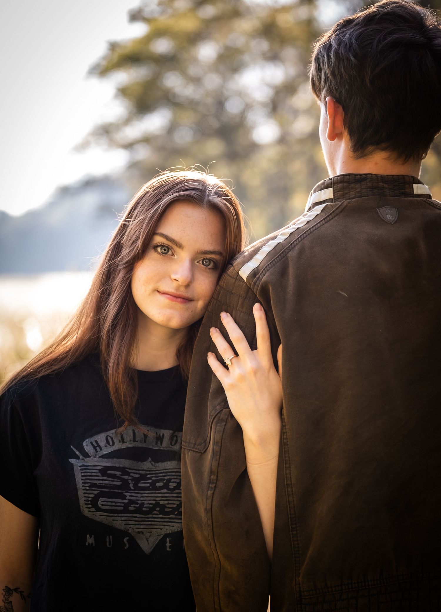 A couple poses together in a romantic outdoor photoshoot with soft natural lighting and autumn scenery.
