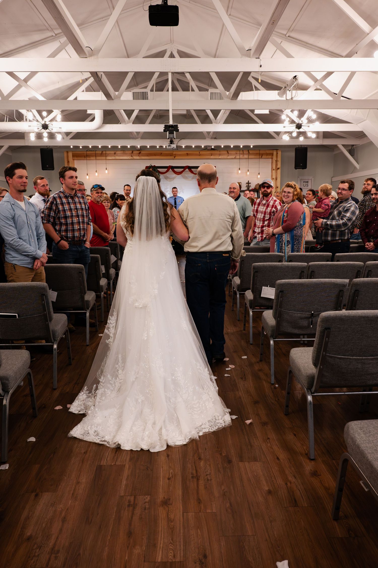 Wedding ceremony venue with wooden floors and rows of grey chairs facing a white gown.
