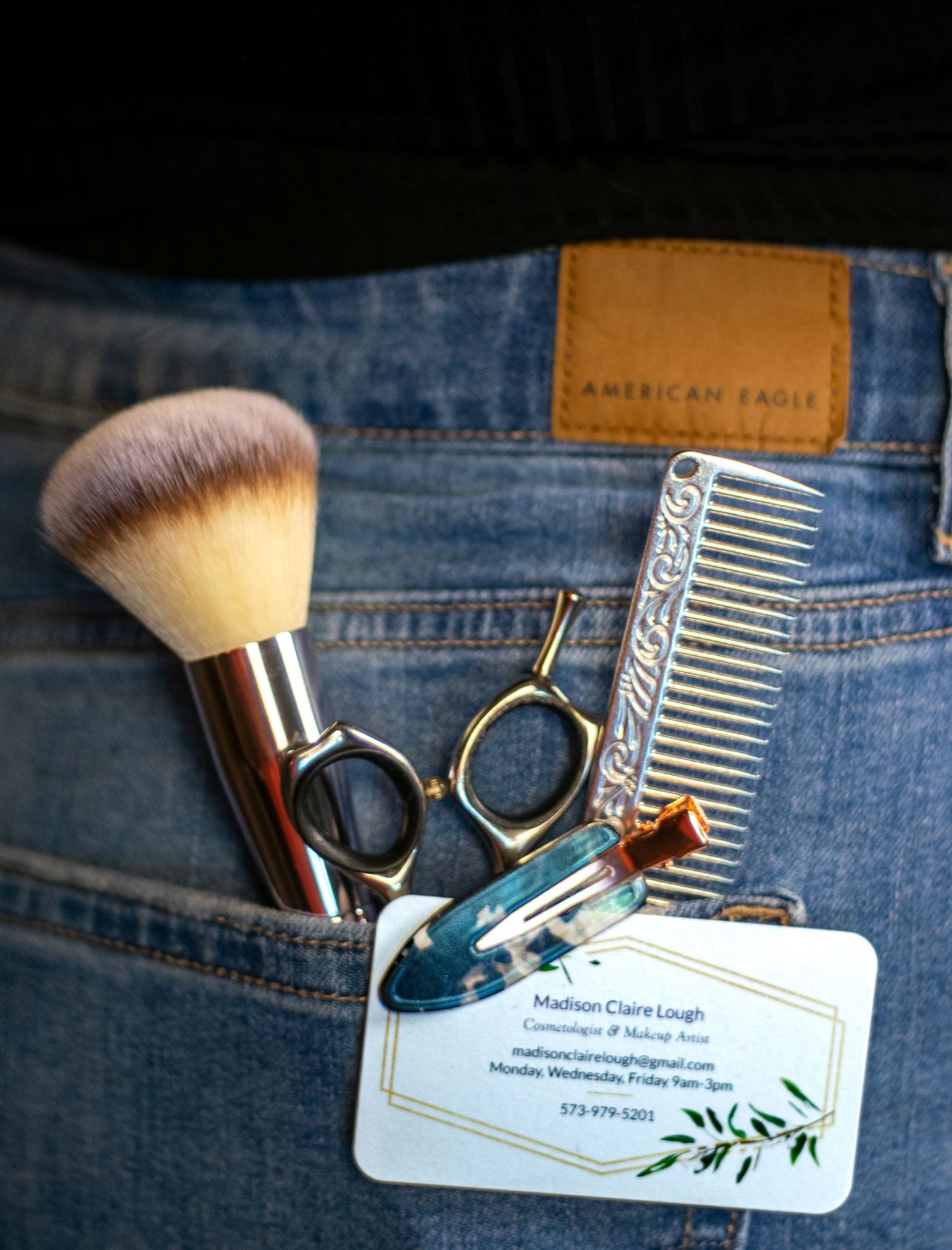 Makeup brushes and business cards with floral designs arranged against denim jeans background.