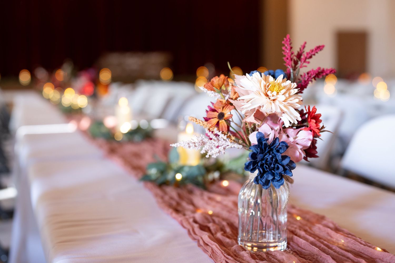 Wedding table decorated with colorful floral arrangements and burgundy accents.