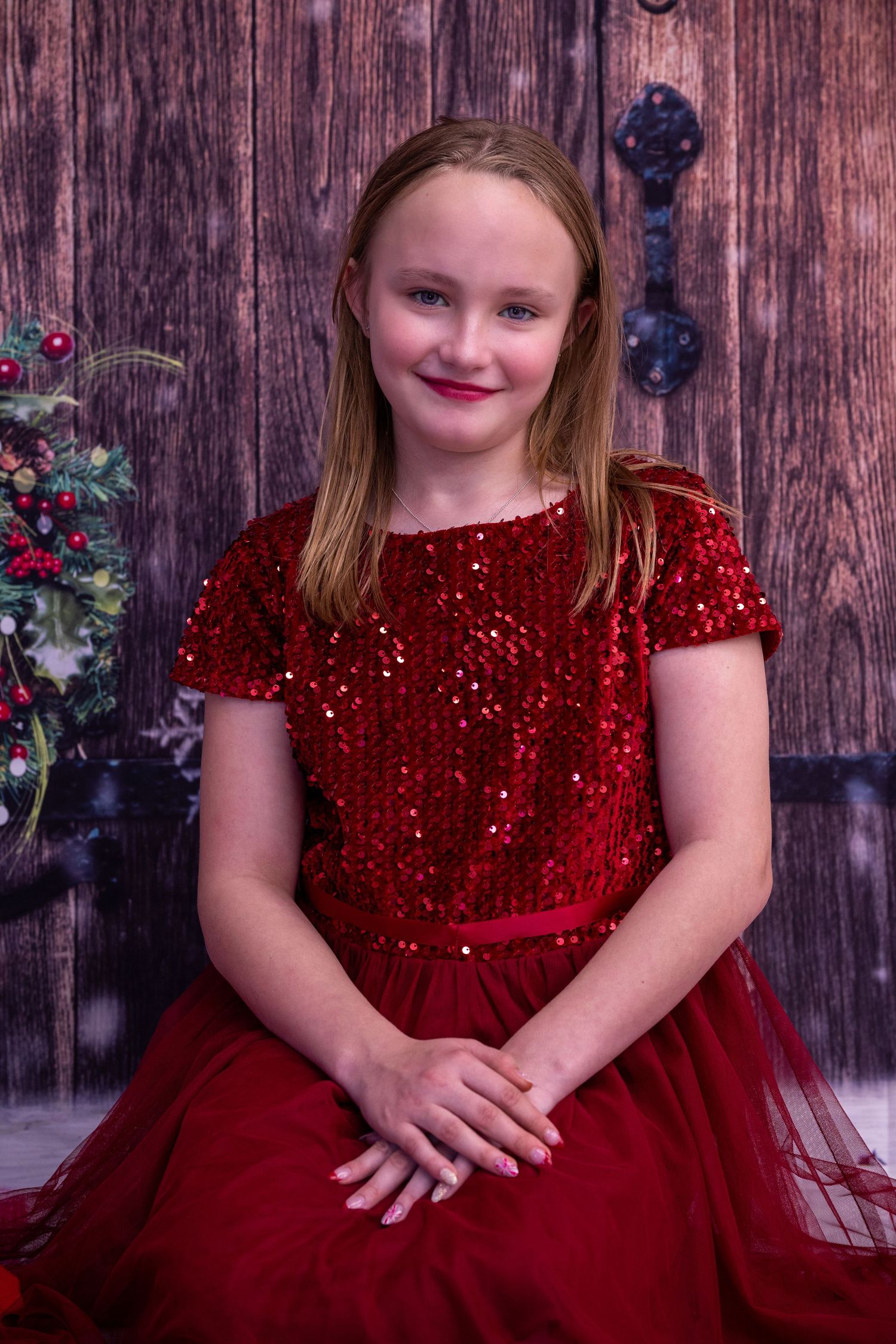 A child in a sparkly red velvet holiday dress with tulle skirt poses against a rustic wooden backdrop.