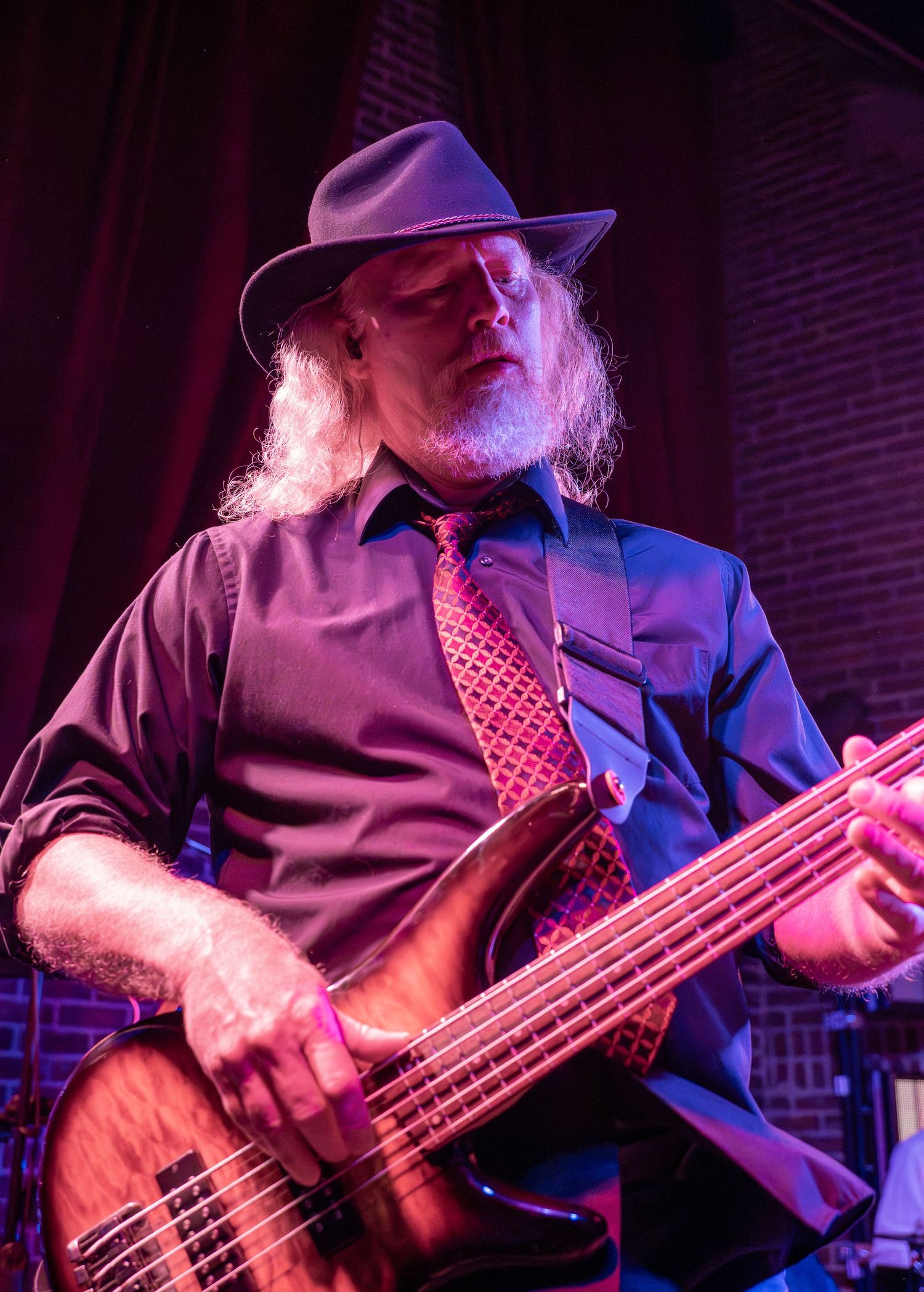 Bass guitarist performs on stage under dramatic purple and blue lighting, creating a moody atmosphere.