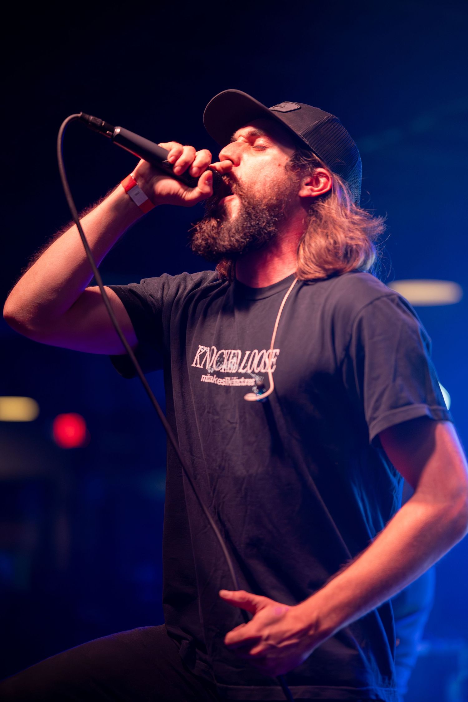 Concert performer in baseball cap singing emotionally into microphone under blue lighting.