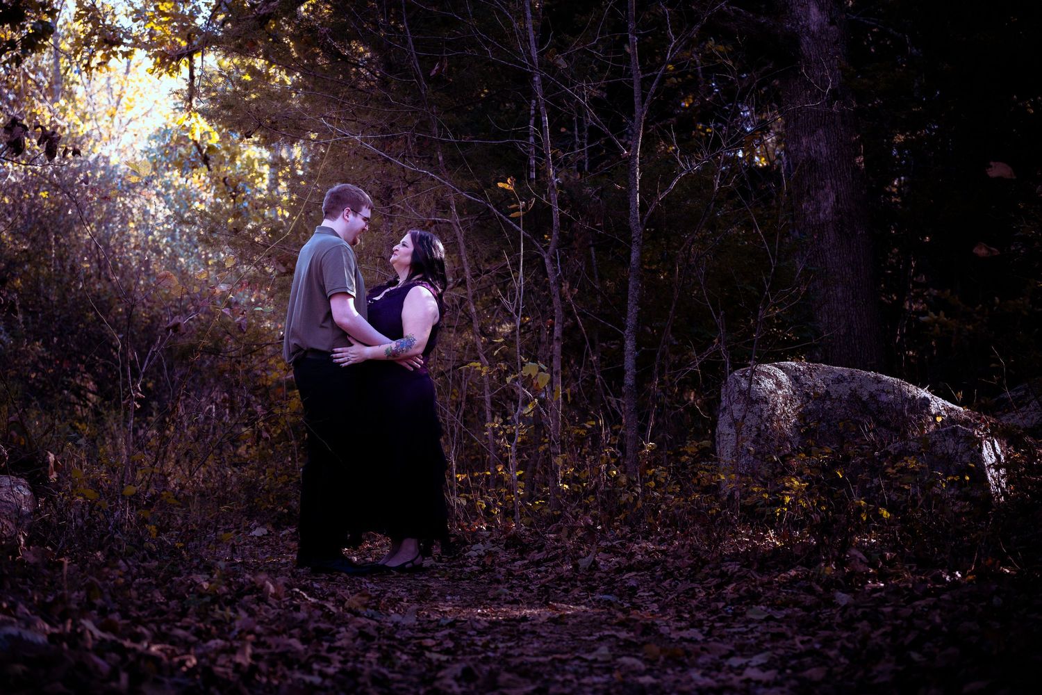 A couple walking together through a wooded path on an autumn day with fallen leaves covering the ground.