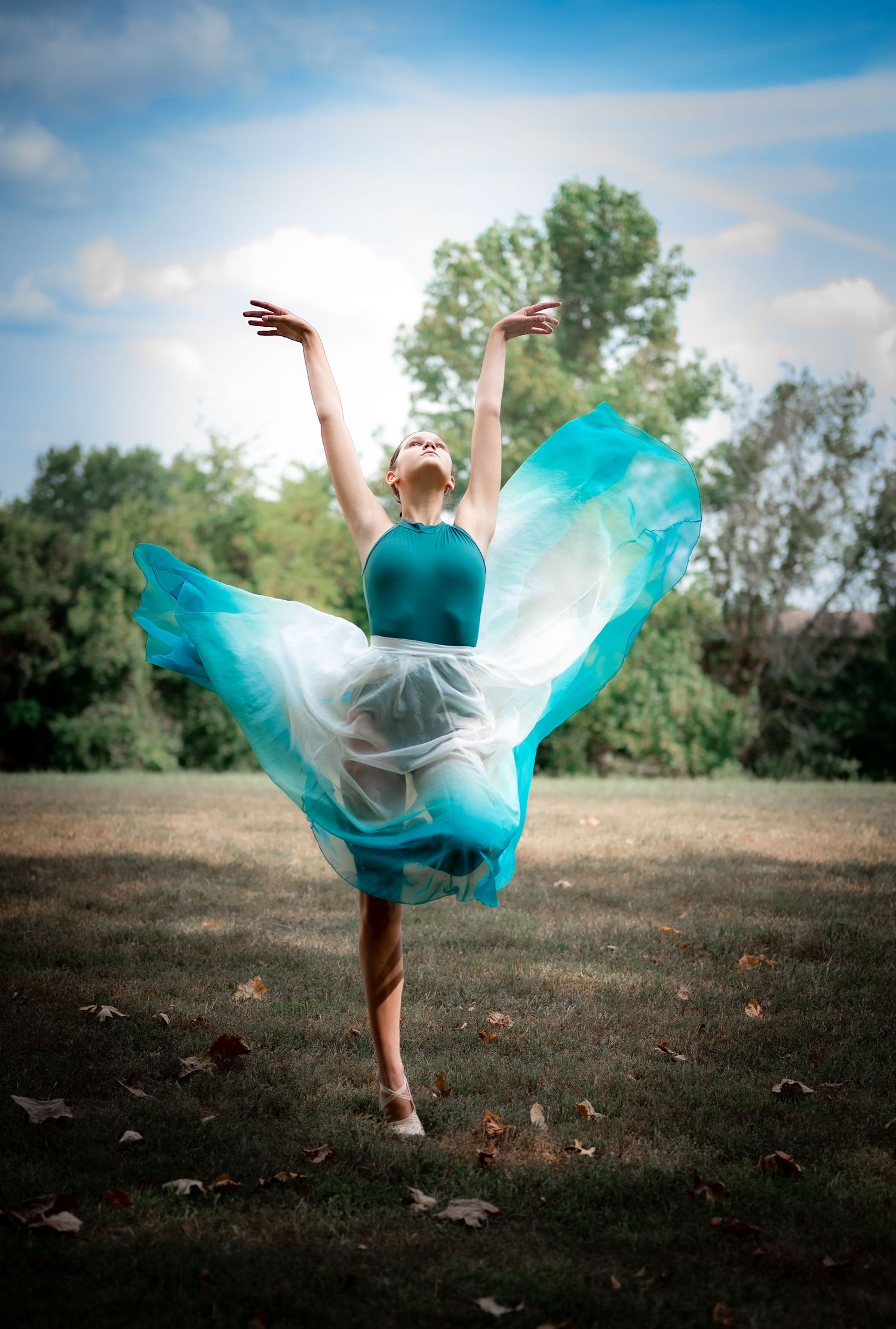 A figure in a flowing turquoise dress twirls gracefully across an autumn field against a bright blue sky.