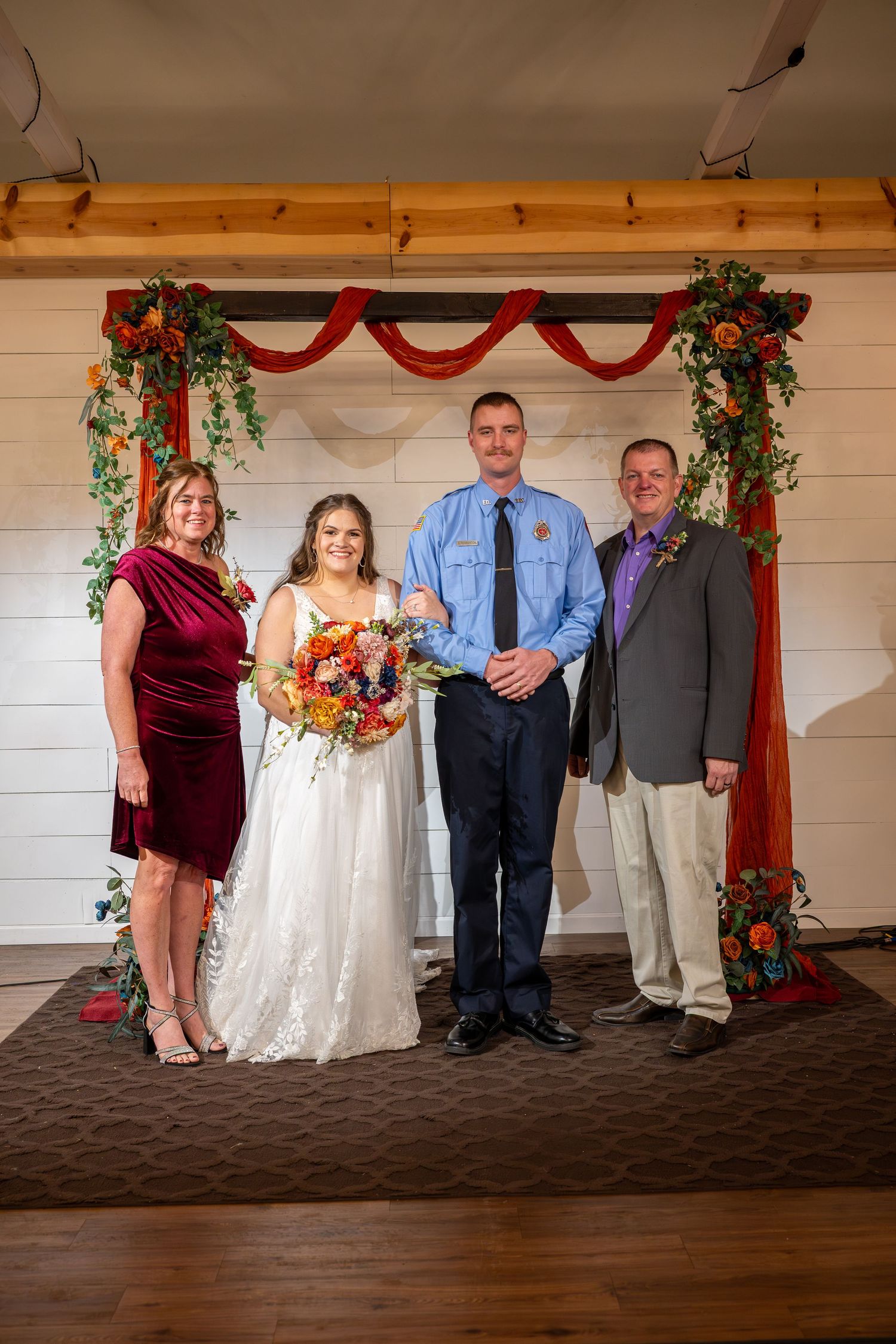 Wedding party poses under decorative red and green arch at indoor venue.