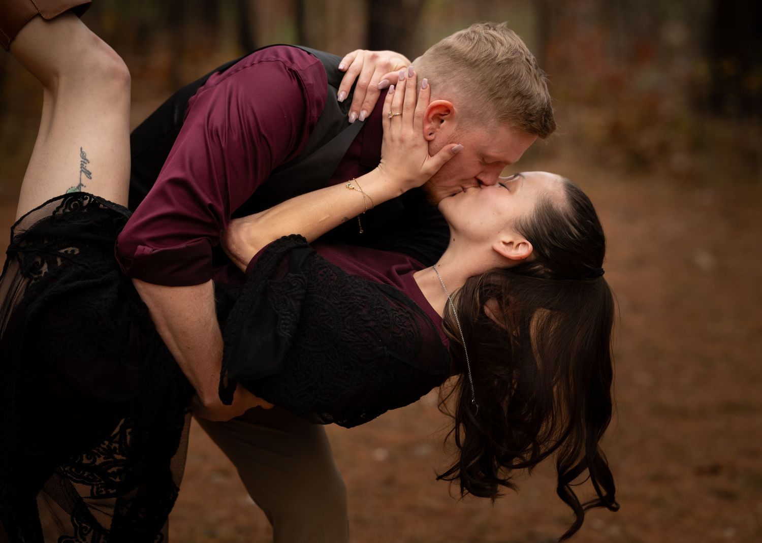 A romantic couple embraces in a dramatic dip pose against an autumn forest backdrop.