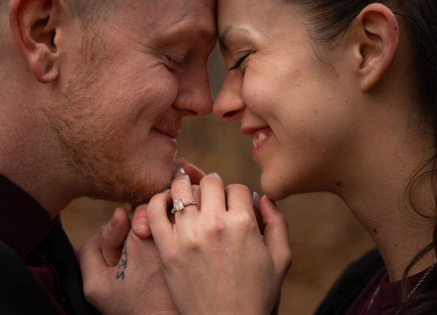 A romantic close-up of a couple touching foreheads and holding hands together while smiling.
