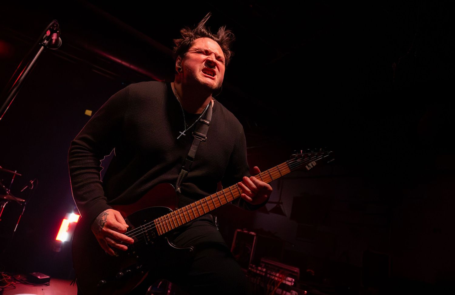 Dark concert photo showing silhouette of guitarist performing under dramatic red lighting.