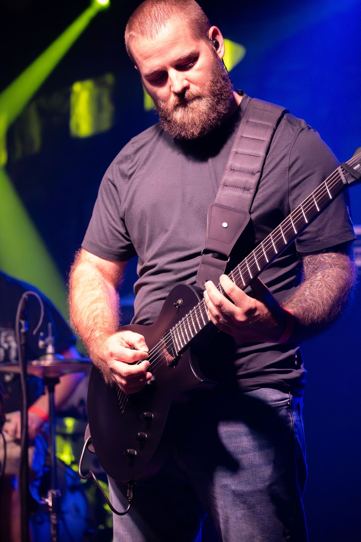 Guitarist in black t-shirt performs on stage with blue lighting and dramatic atmosphere.