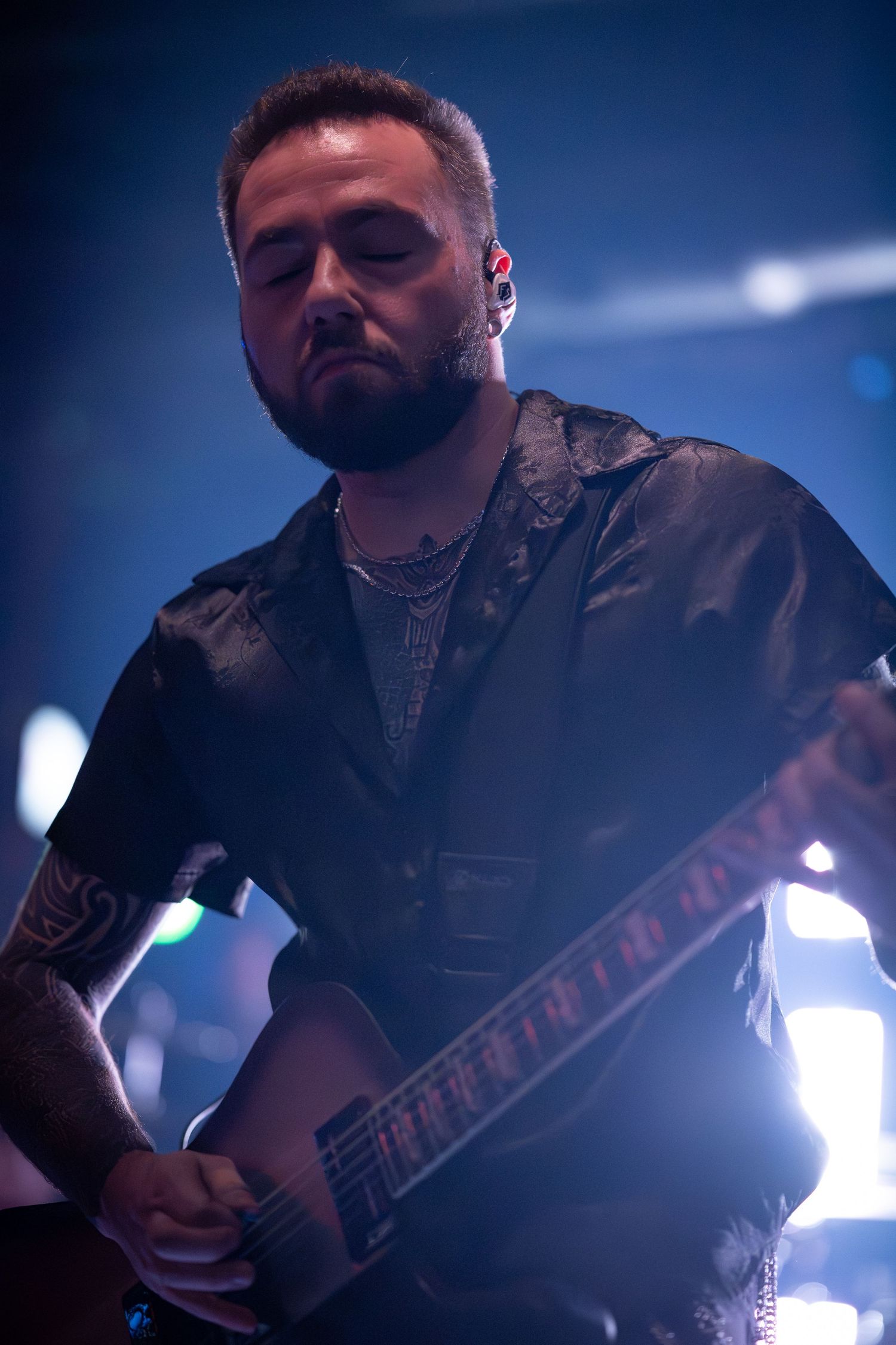 Guitarist performs on stage in dramatic blue lighting while playing an electric guitar during a concert performance.