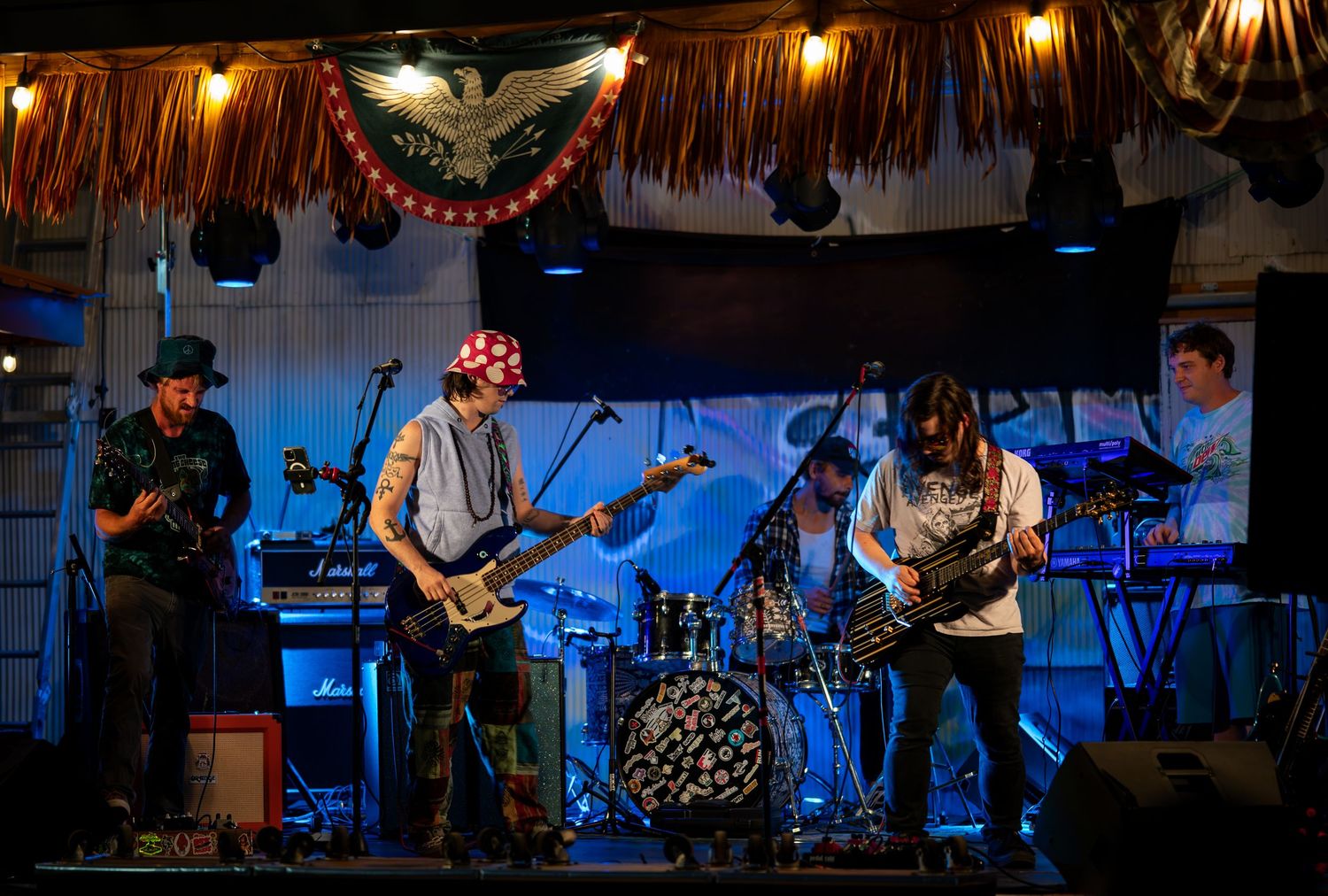 Musicians perform on stage with guitars and drums under dramatic lighting at a live concert venue.