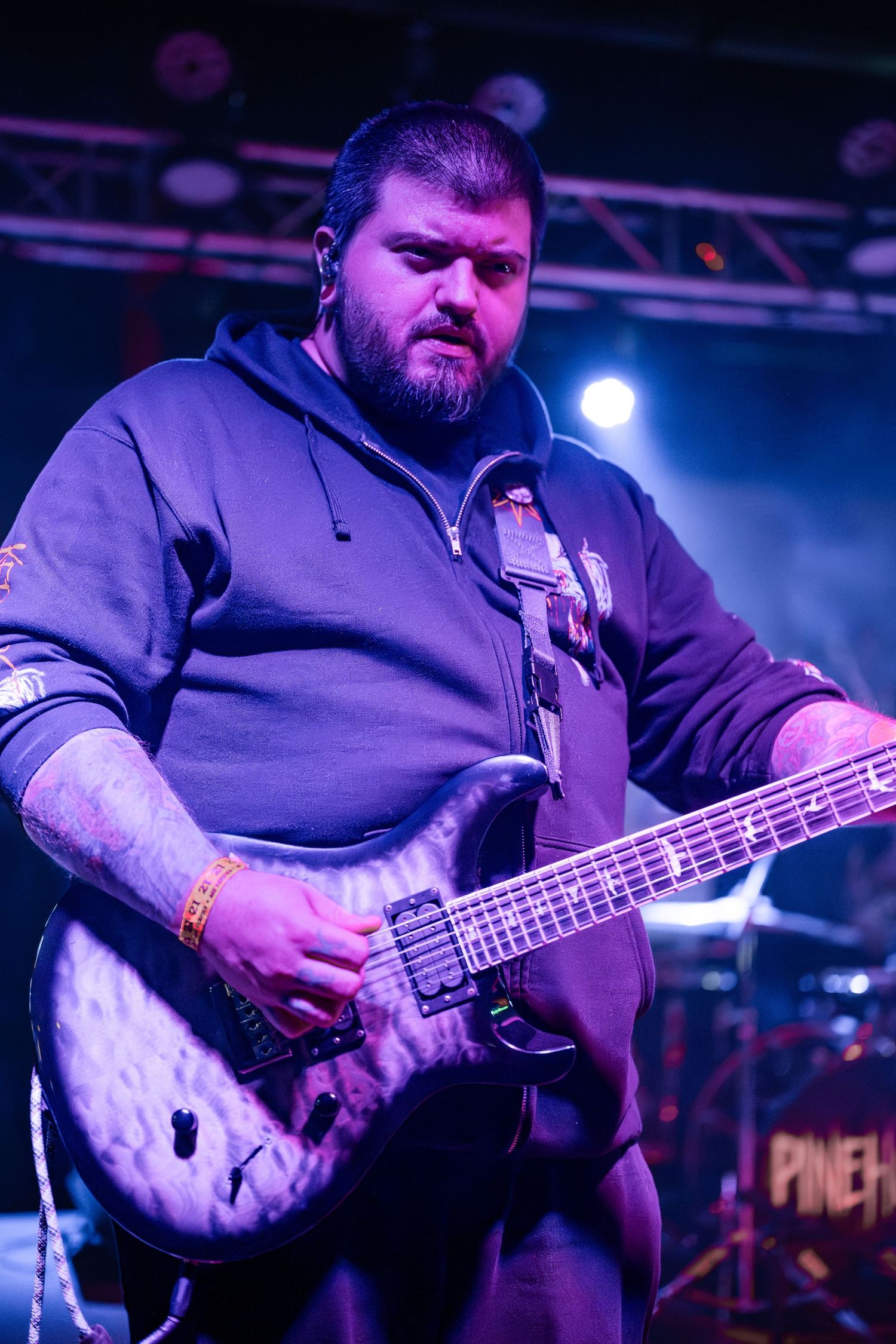 Bass guitarist performs on stage with quilted maple bass guitar under blue stage lighting.