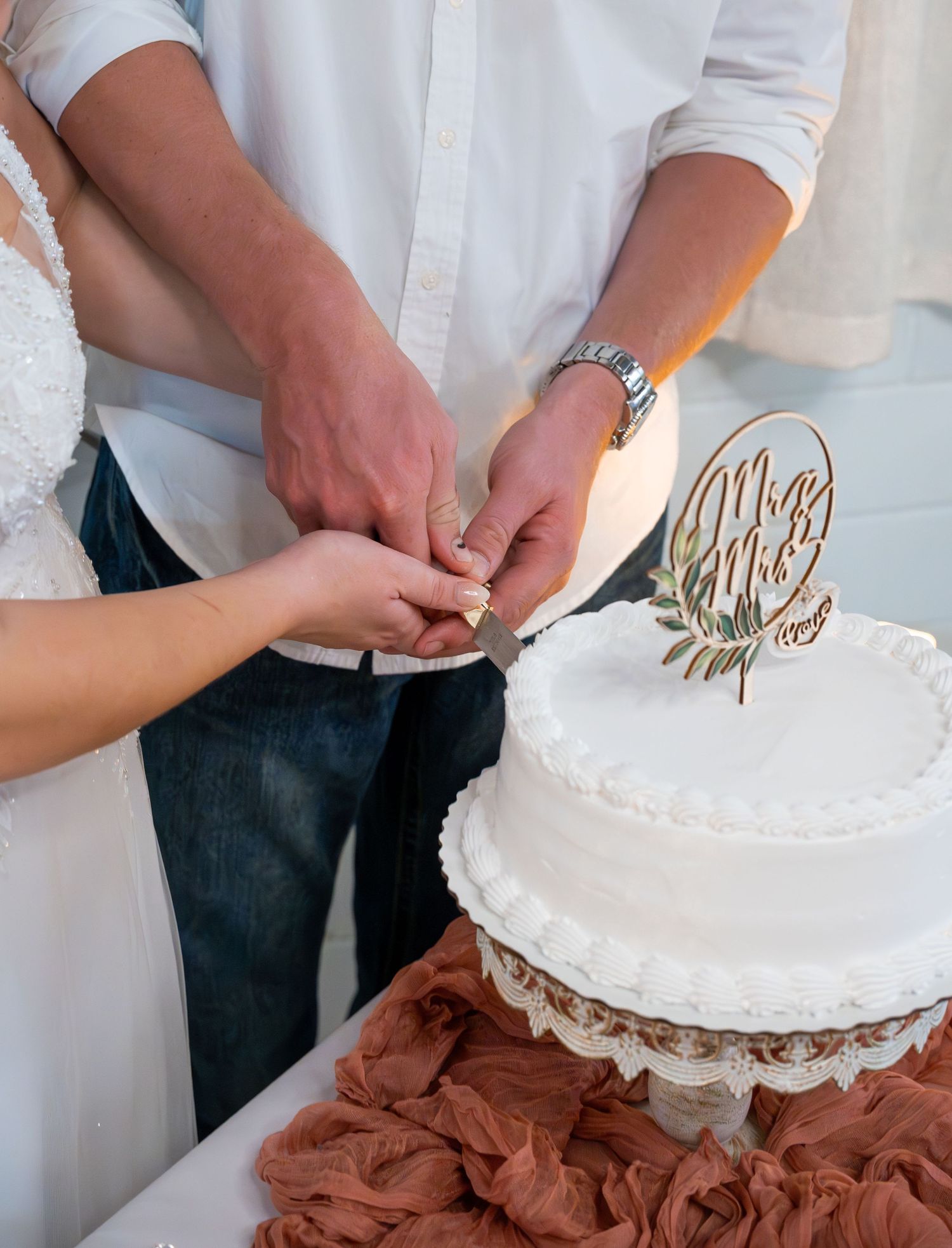 Close-up shots of hands cutting a white wedding cake decorated with metallic accents.