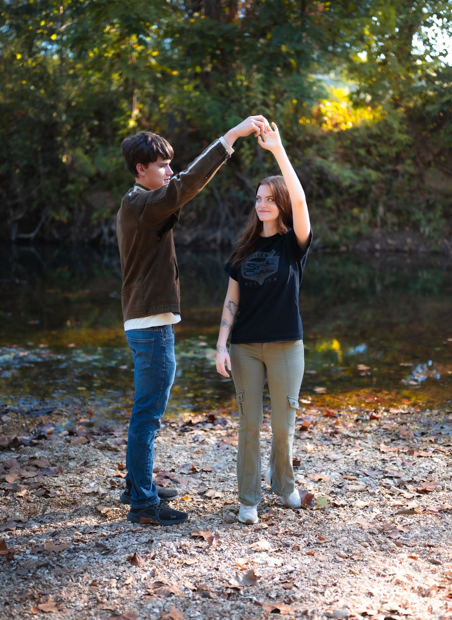 Two people dance together on fallen autumn leaves by a tranquil lake on a sunny afternoon.