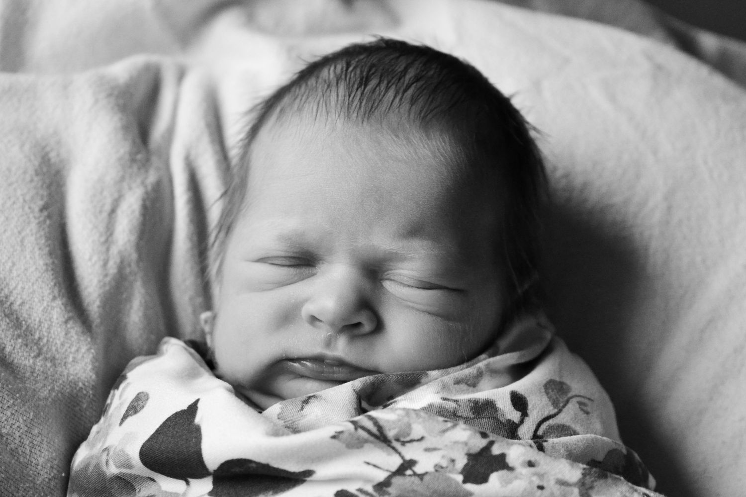 A sleeping newborn baby wrapped in a white blanket rests peacefully on soft bedding.