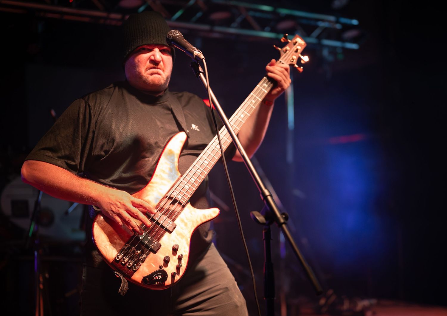Bass guitarist performs on stage with a black t-shirt under dramatic blue concert lighting.