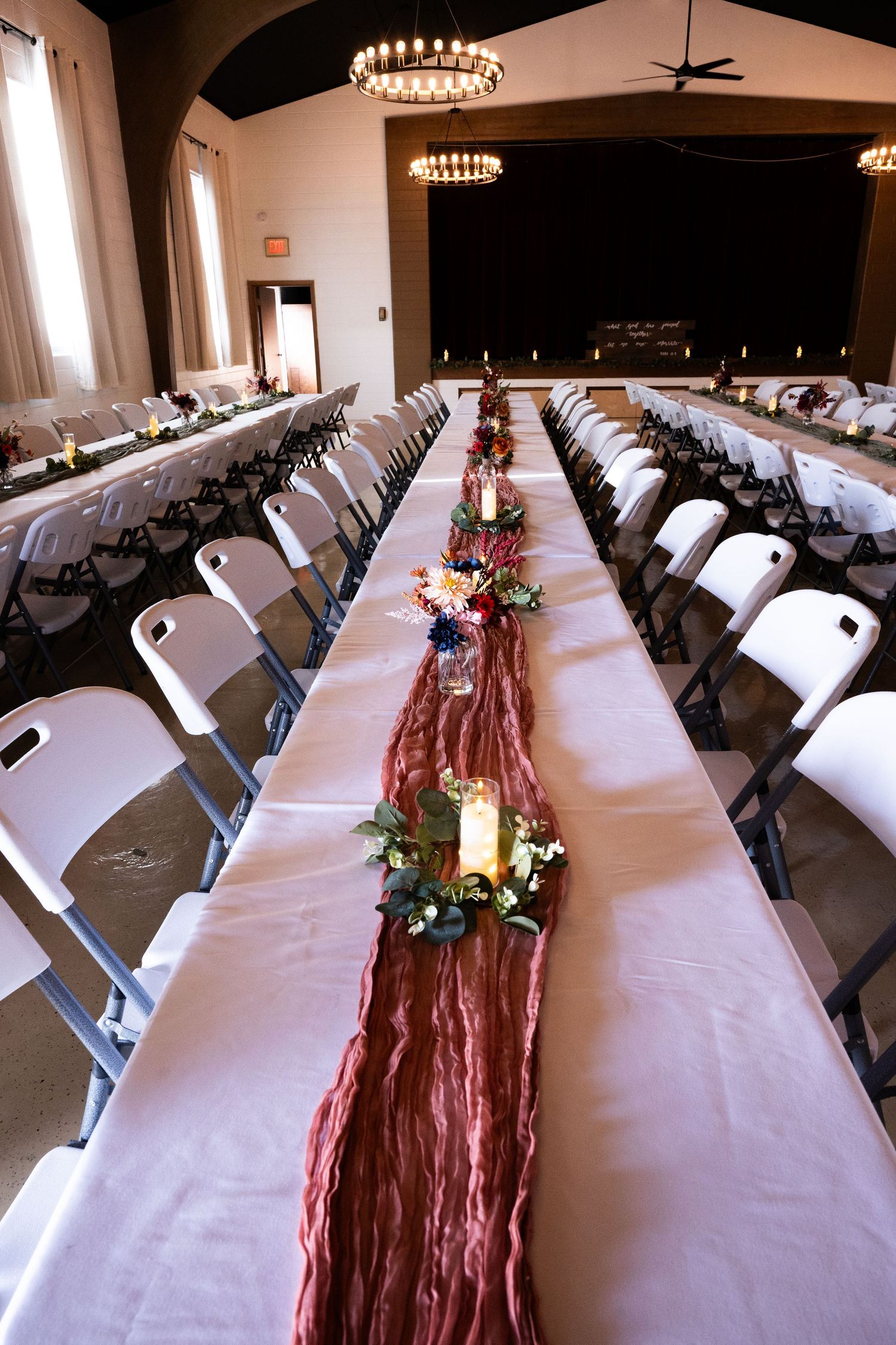 Long reception tables with white tablecloths and burgundy runners decorated with floral centerpieces.