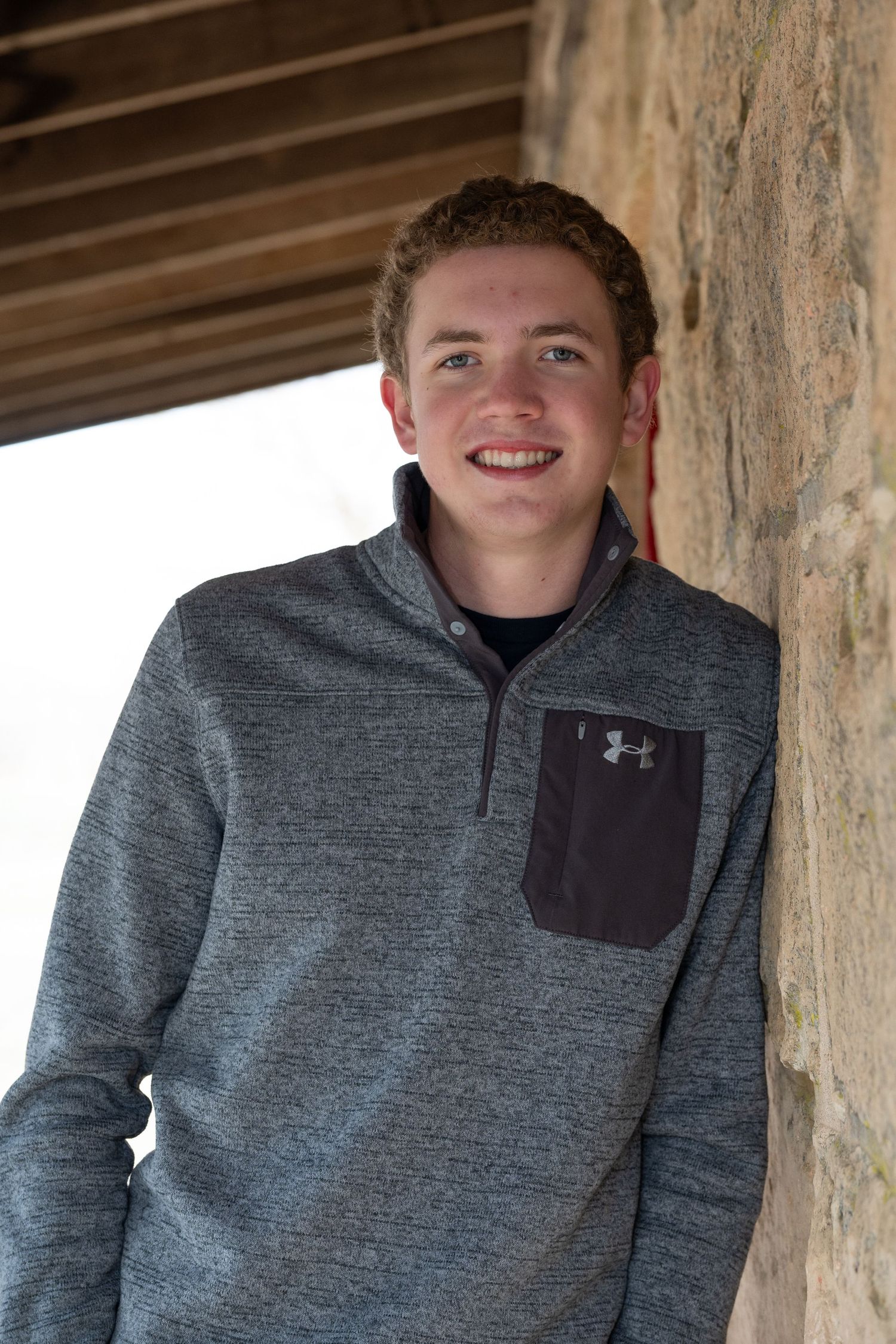 Person wearing grey fleece pullover smiling against stone wall background.