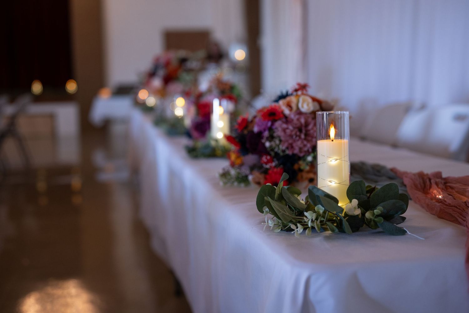 Elegant table settings with candles and greenery decorations at a wedding reception.