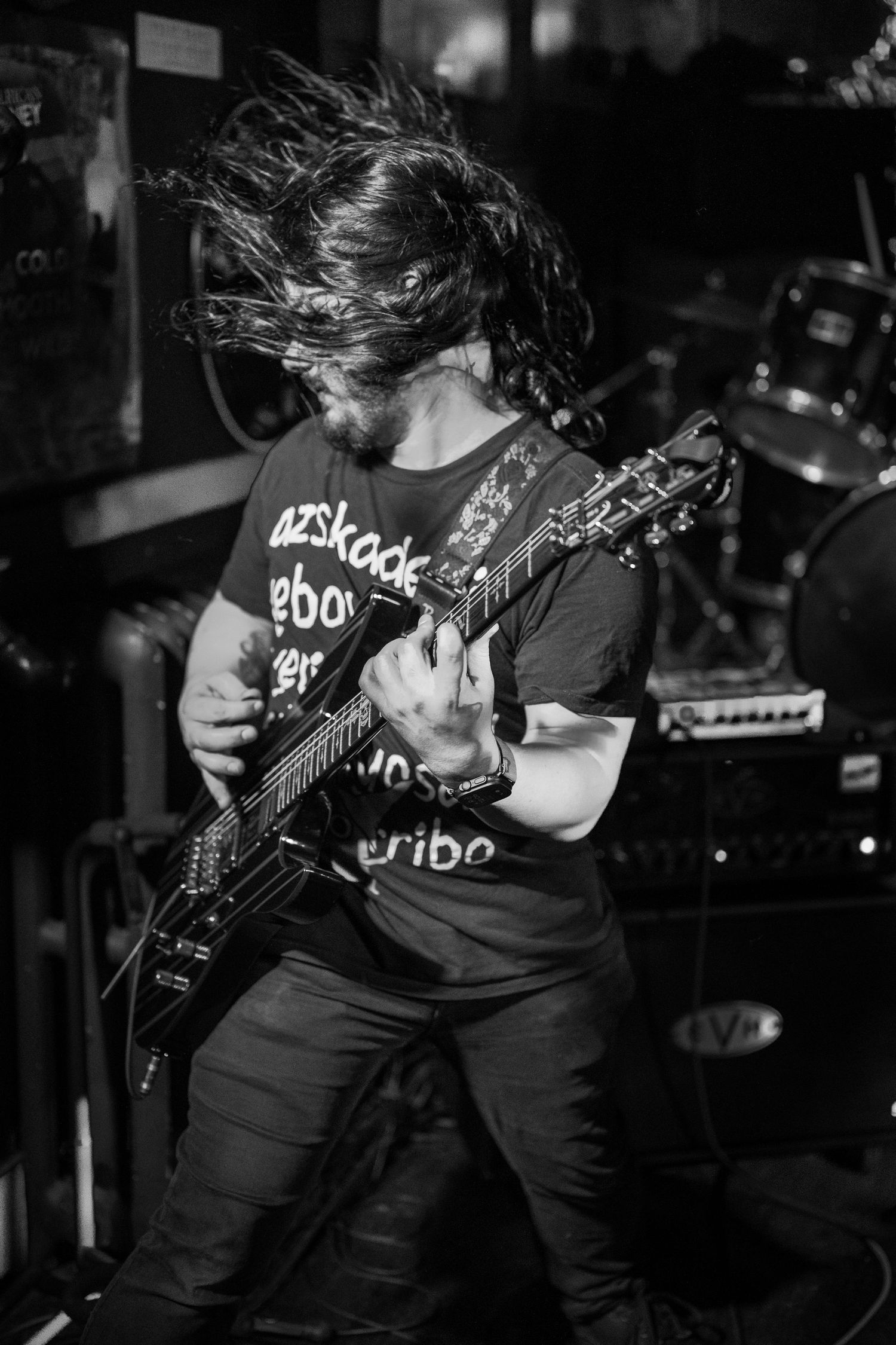 Black and white photo of a guitarist headbanging while playing electric guitar on stage during a live rock performance.