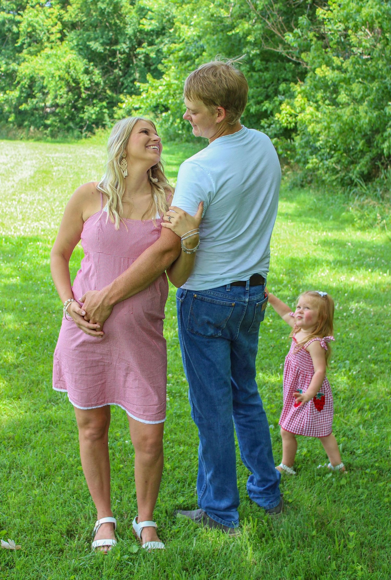A family in matching pink and blue outfits poses together playfully on a grassy lawn surrounded by green trees.