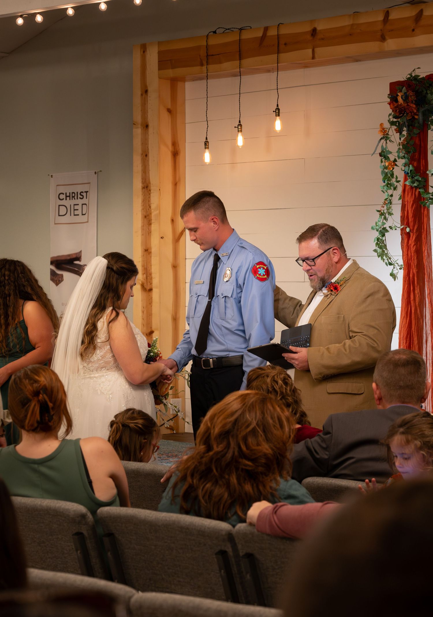 Indoor wedding ceremony with wooden beam decor and string lights overhead.