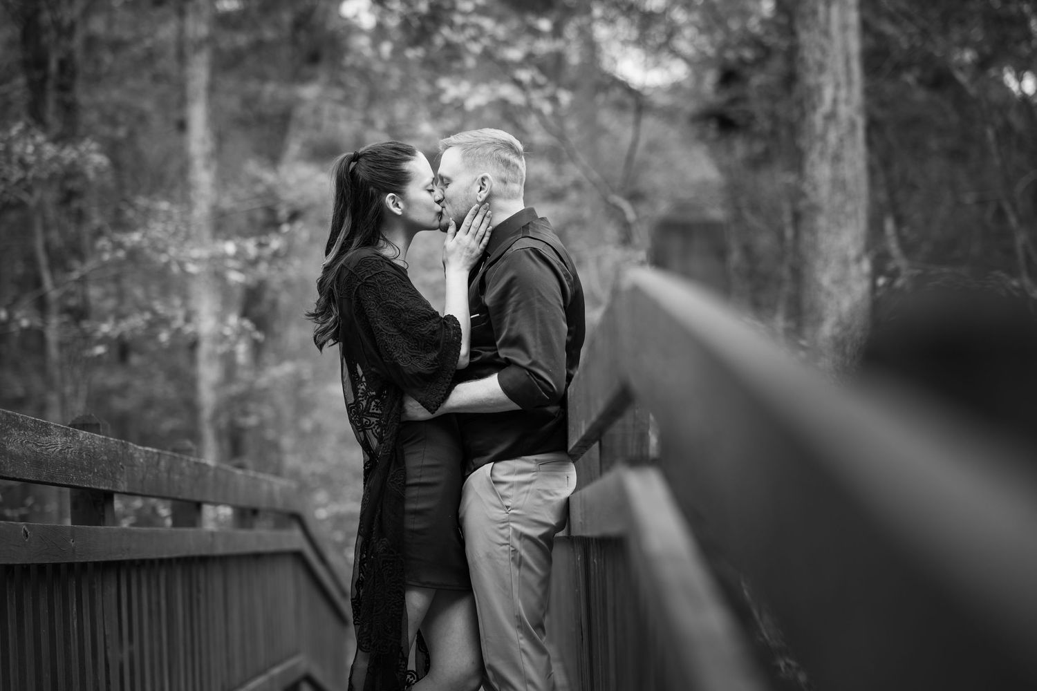 A couple shares a romantic moment during a black and white engagement photoshoot in an outdoor setting.