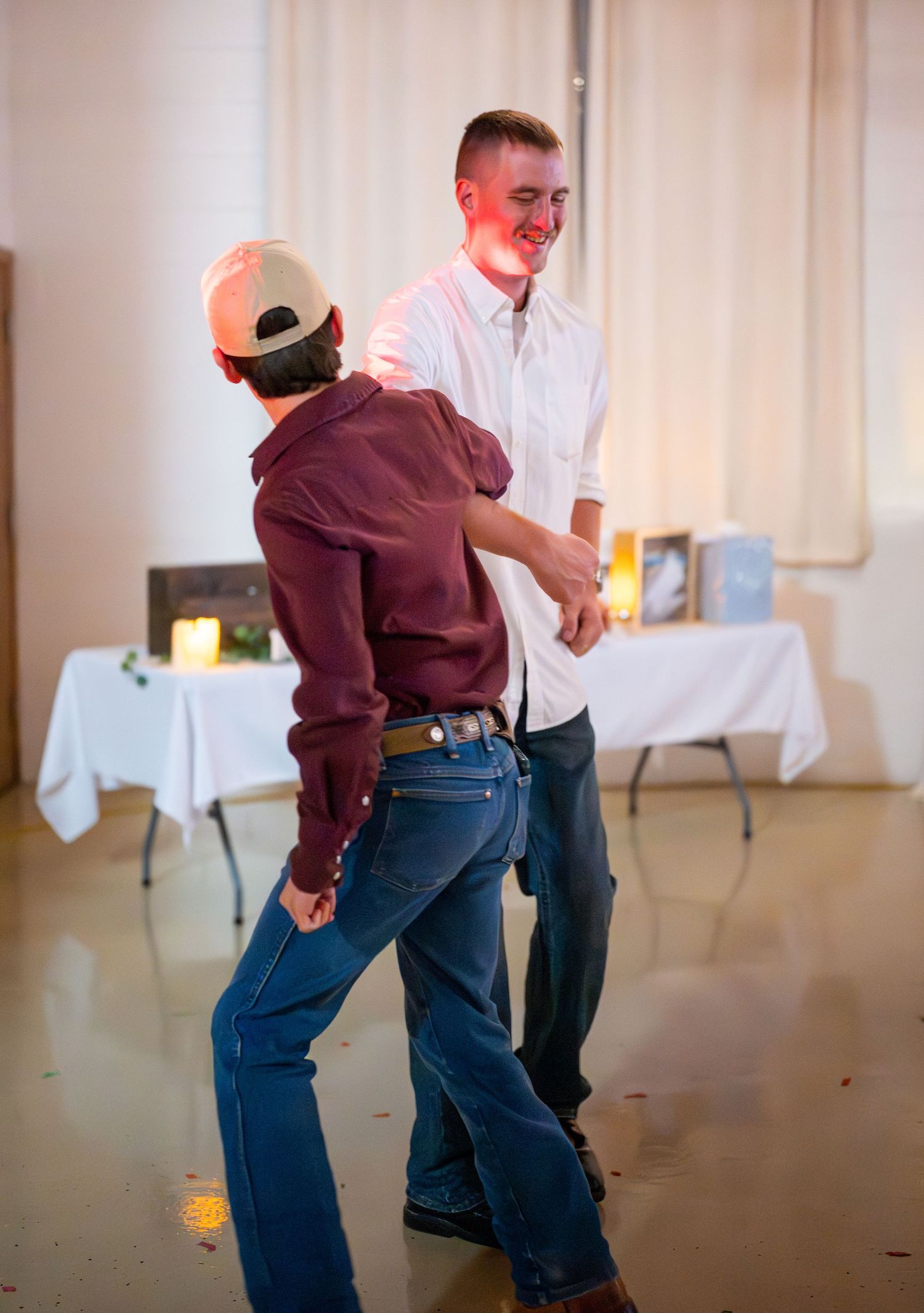 Wedding reception guests dancing energetically in a hall with white curtains.