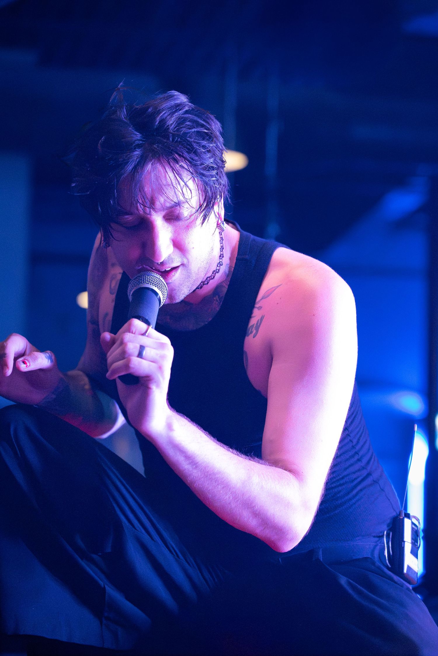 Close-up of performer singing emotionally into microphone under dramatic blue stage lighting.