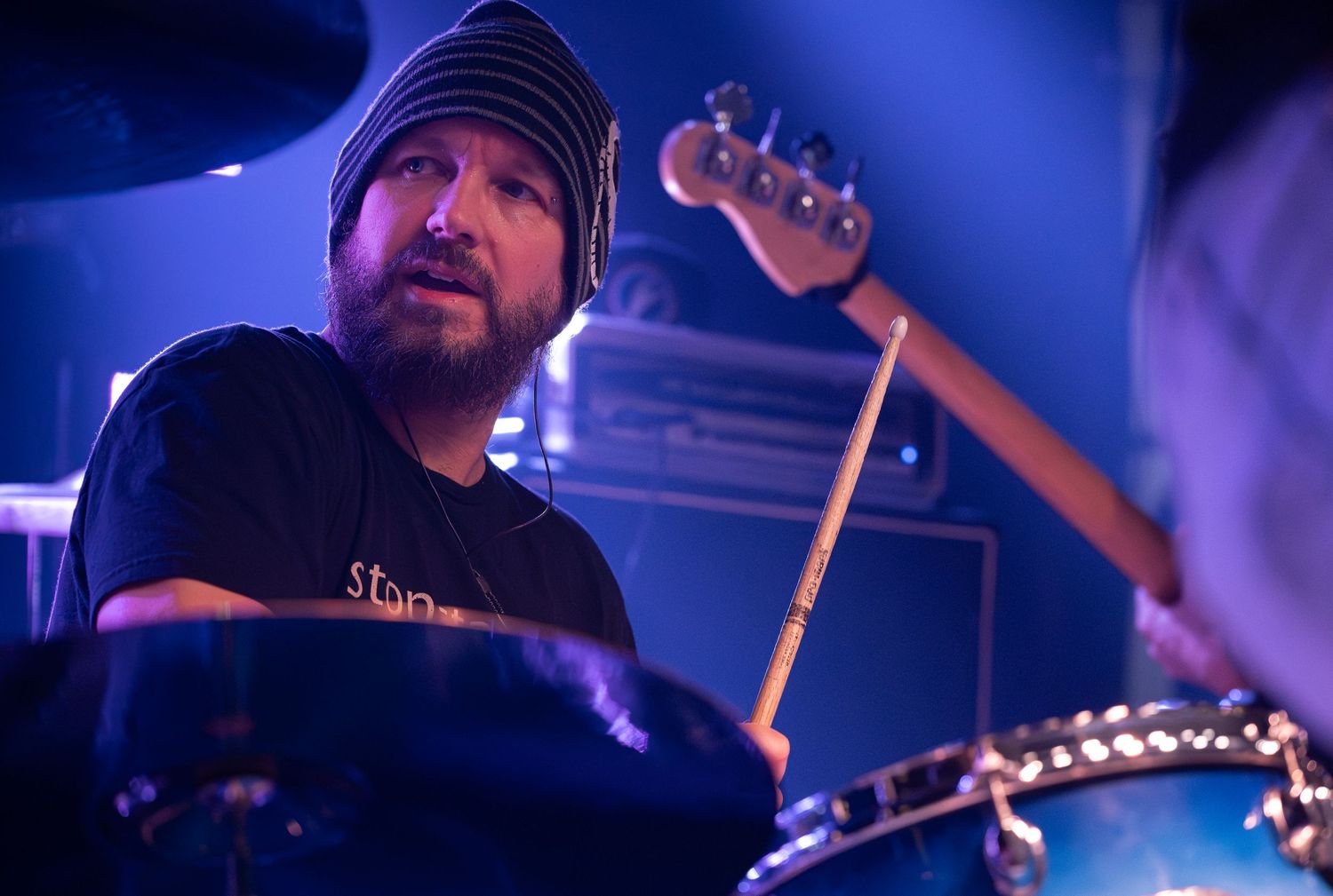 Band members playing instruments on dimly lit stage with blue lighting effects.