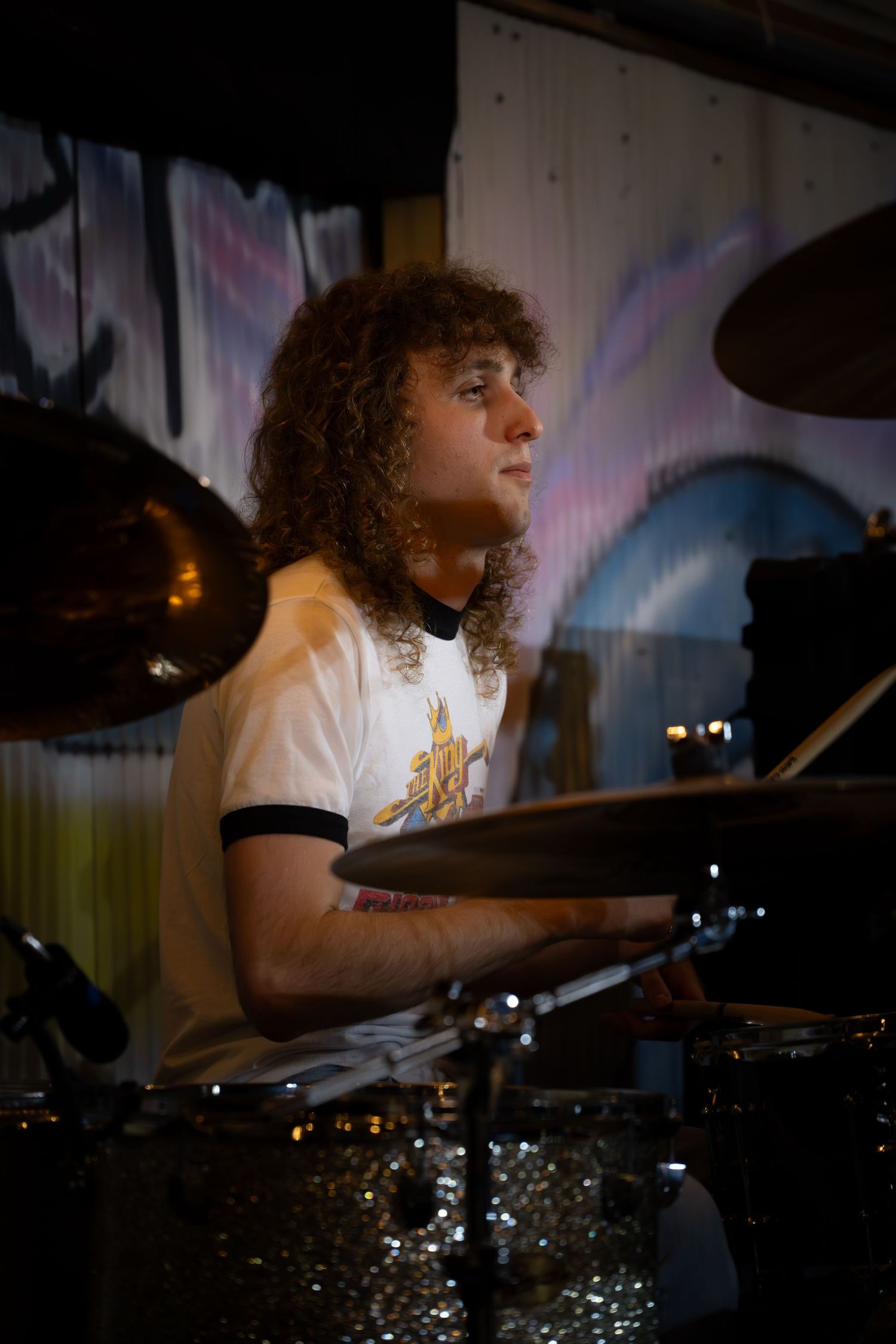 A drummer performs with intense focus behind a drum kit in a dimly lit venue, captured in a series of motion shots.