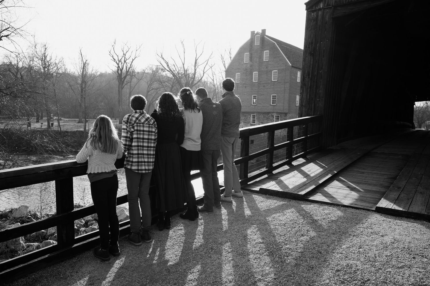 Silhouetted figures stand along a railing at sunset, casting long shadows across the ground.