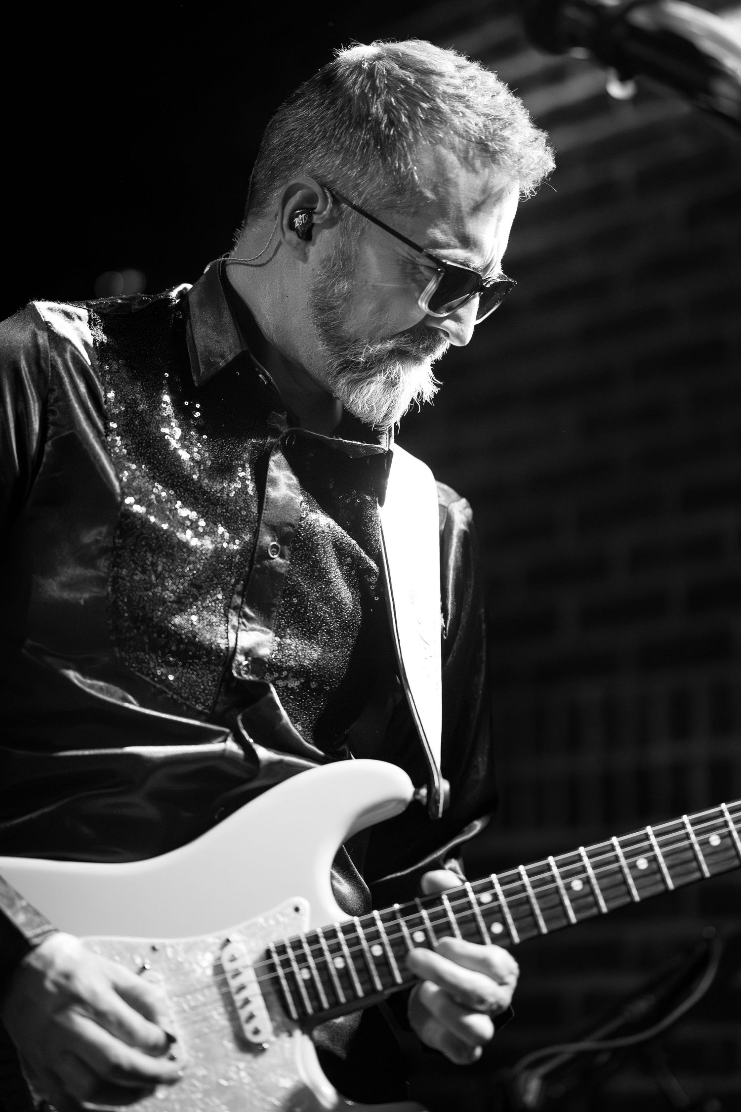 A musician plays an acoustic guitar in black and white, shown in a series of close-up shots focusing on their hands and instrument.