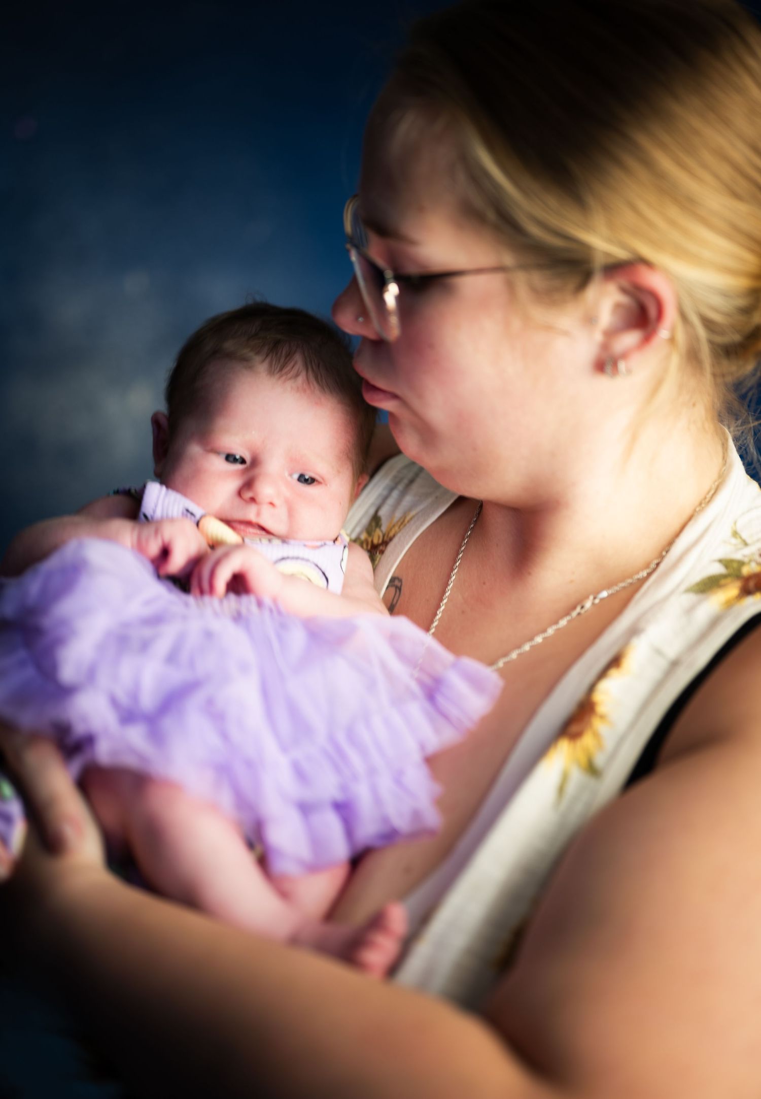 A tender moment between parent and infant wearing a purple tulle dress in soft lighting.