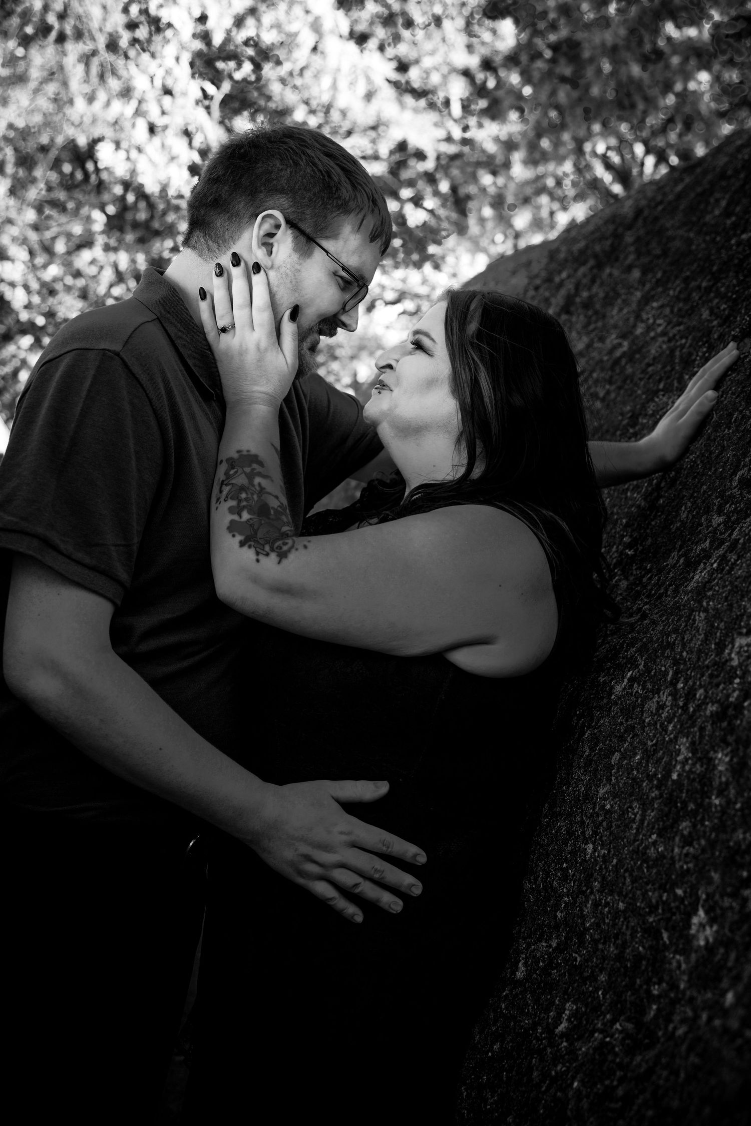 A romantic black and white photo series of a couple embracing against a tree trunk in dappled sunlight.