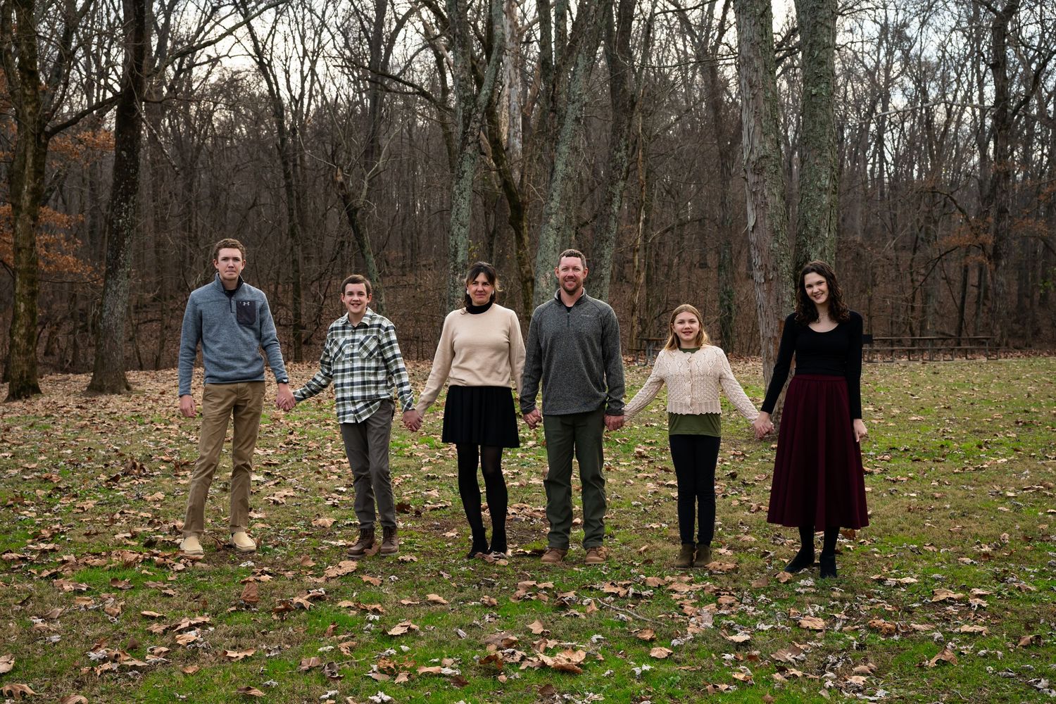 Family group standing in line among autumn trees and fallen leaves.
