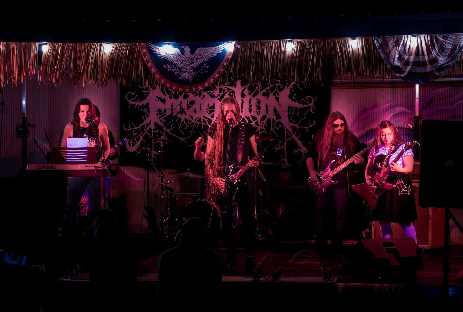 A metal band performs on a dimly lit stage with red and purple lighting during a live concert.