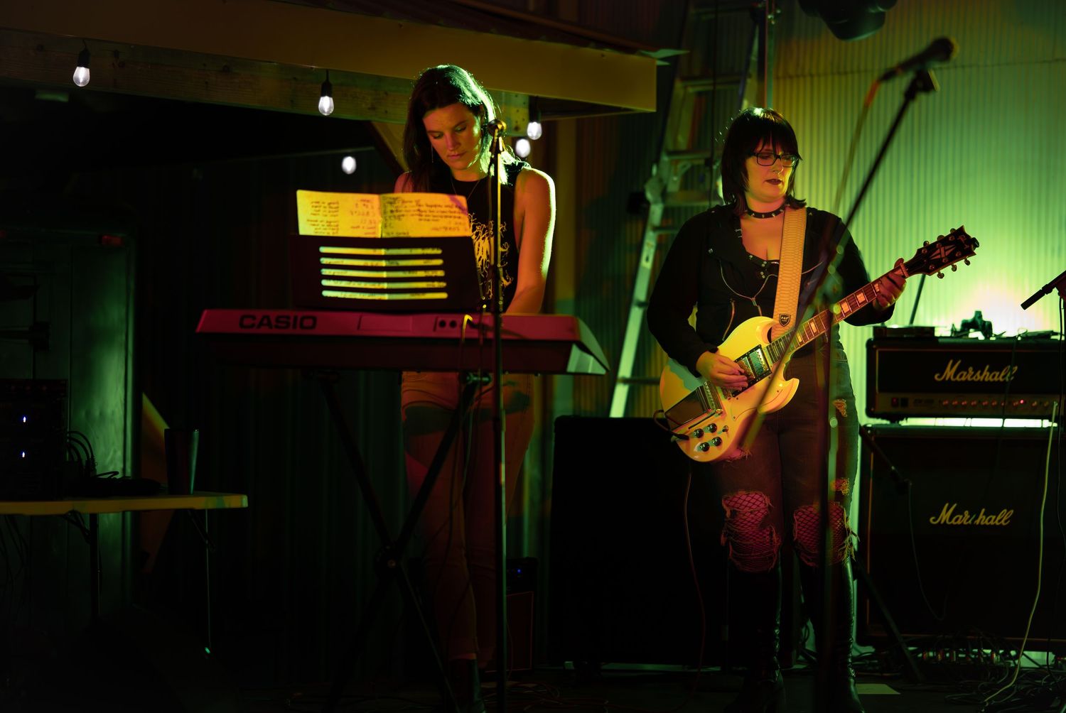 Musicians perform on stage in a dimly lit venue with green lighting and various instruments visible.