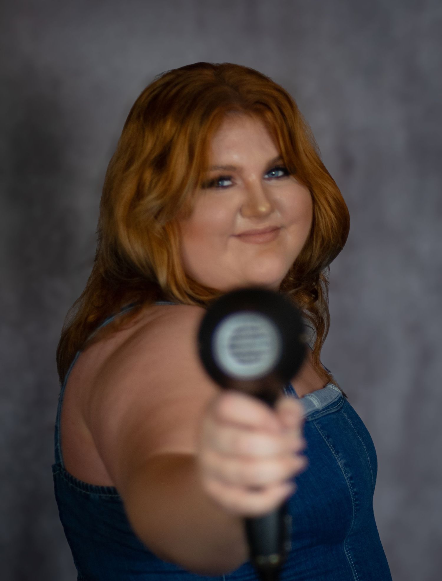 A person with red hair in a blue top holds and points a microphone in a sequence of similar poses against a gray backdrop.