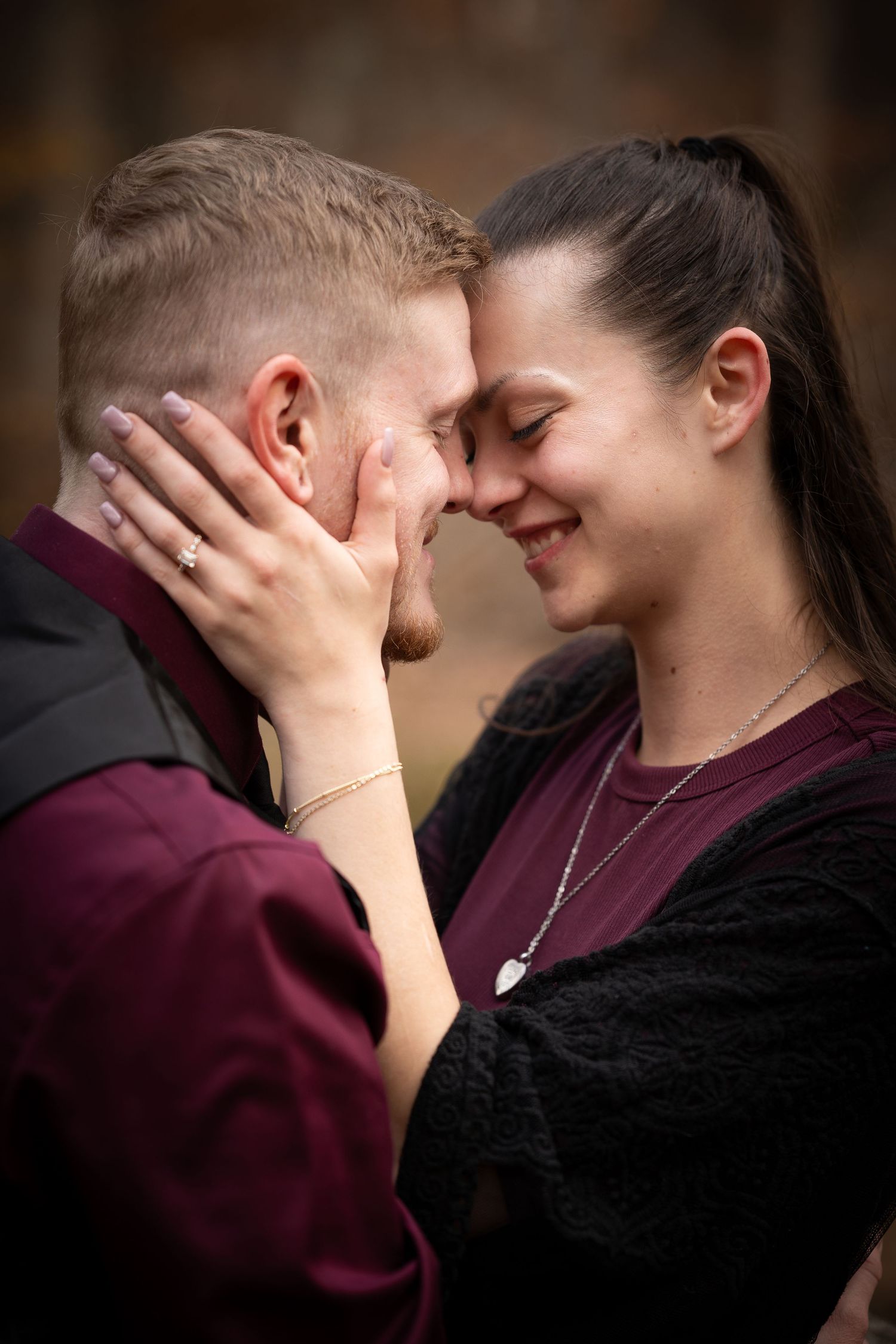 A couple shares an intimate moment in burgundy and black clothing against a dark background.