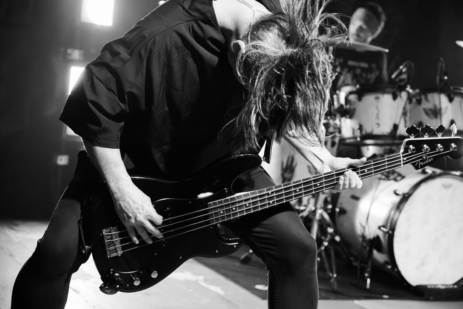Black and white photo of musicians performing with guitars and drum kit on stage.