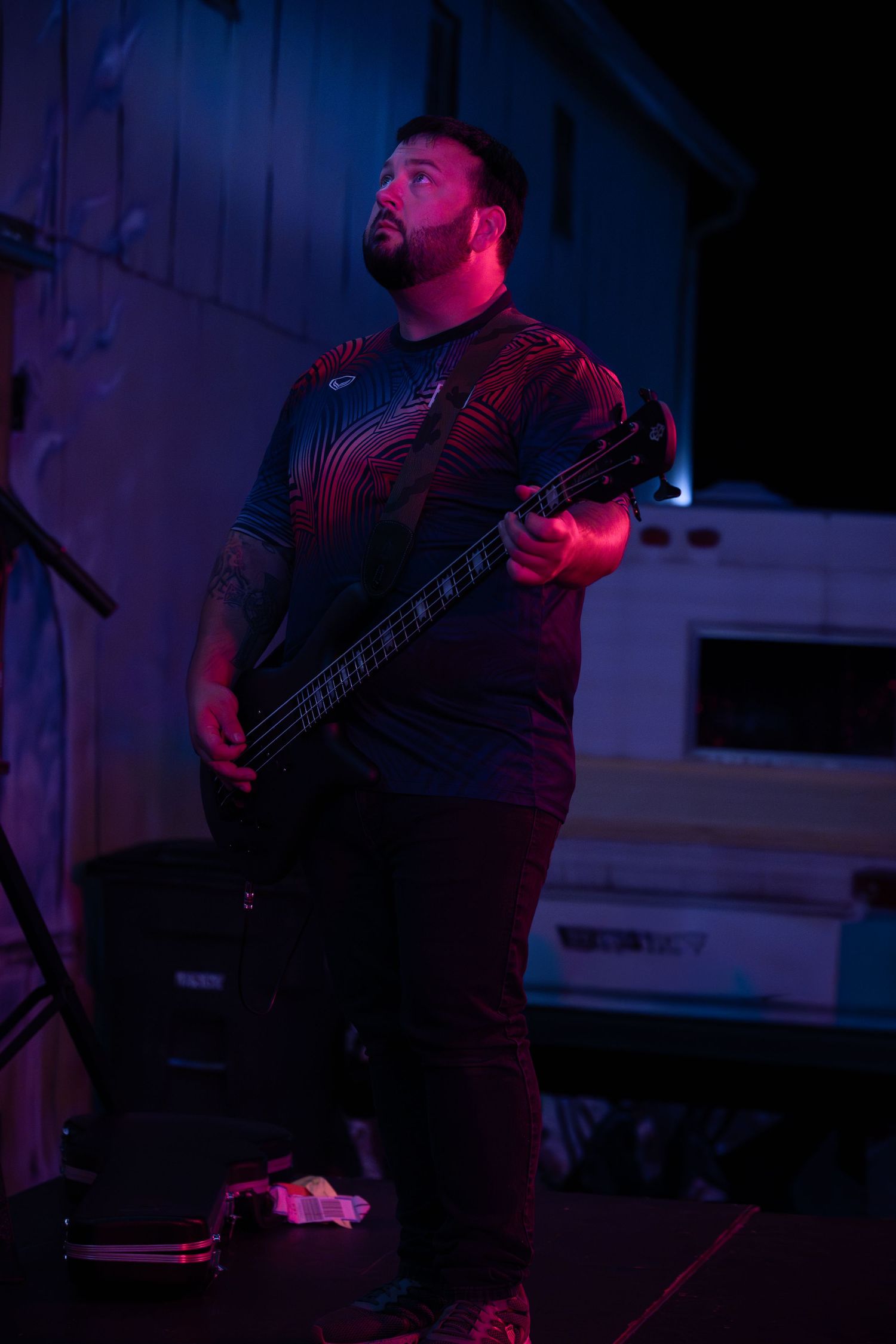 Bass player performing on stage illuminated by dramatic red and blue lighting during a live music performance.