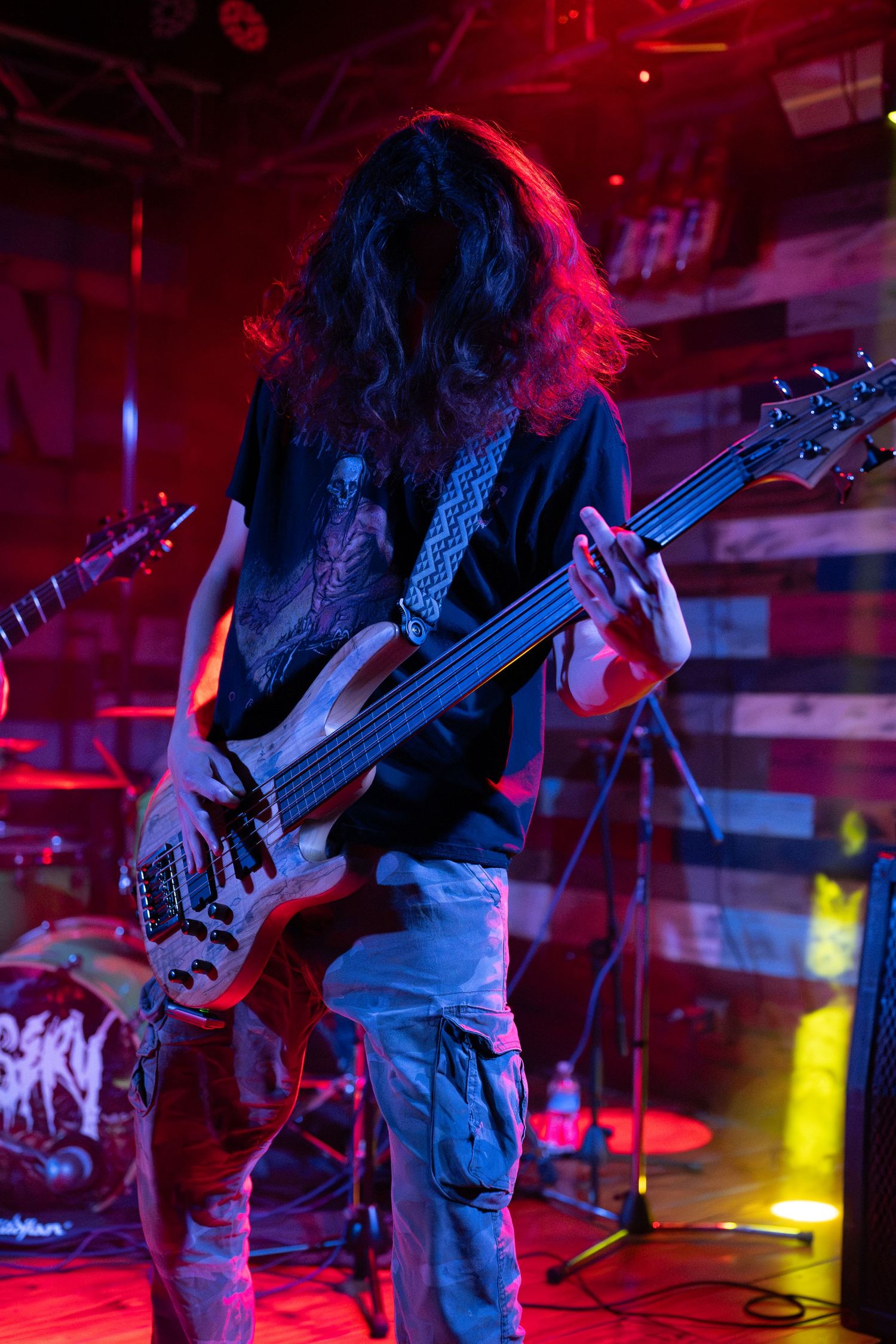 Long-haired guitarist performs on stage under dramatic red and blue lighting at a live metal concert.