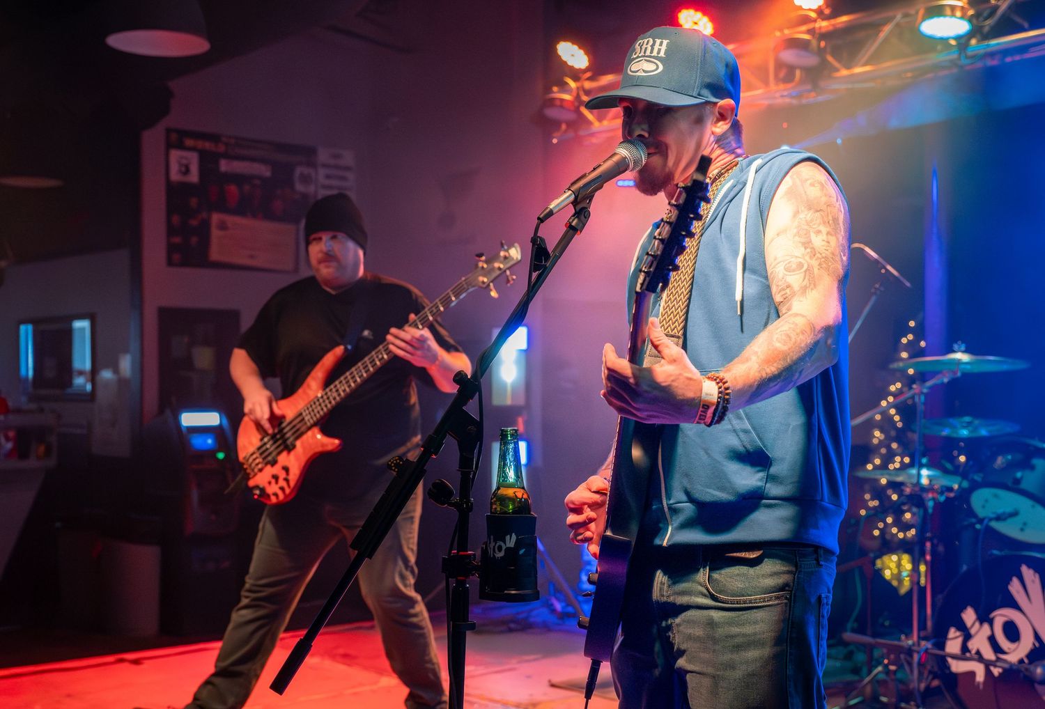 Musicians perform on stage with colorful red and blue lighting effects during a live rock concert performance.