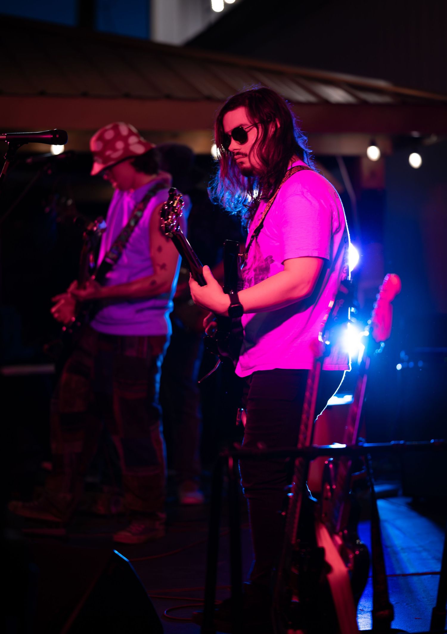 Band performs on dark stage illuminated by blue and pink lights during an energetic live music performance.