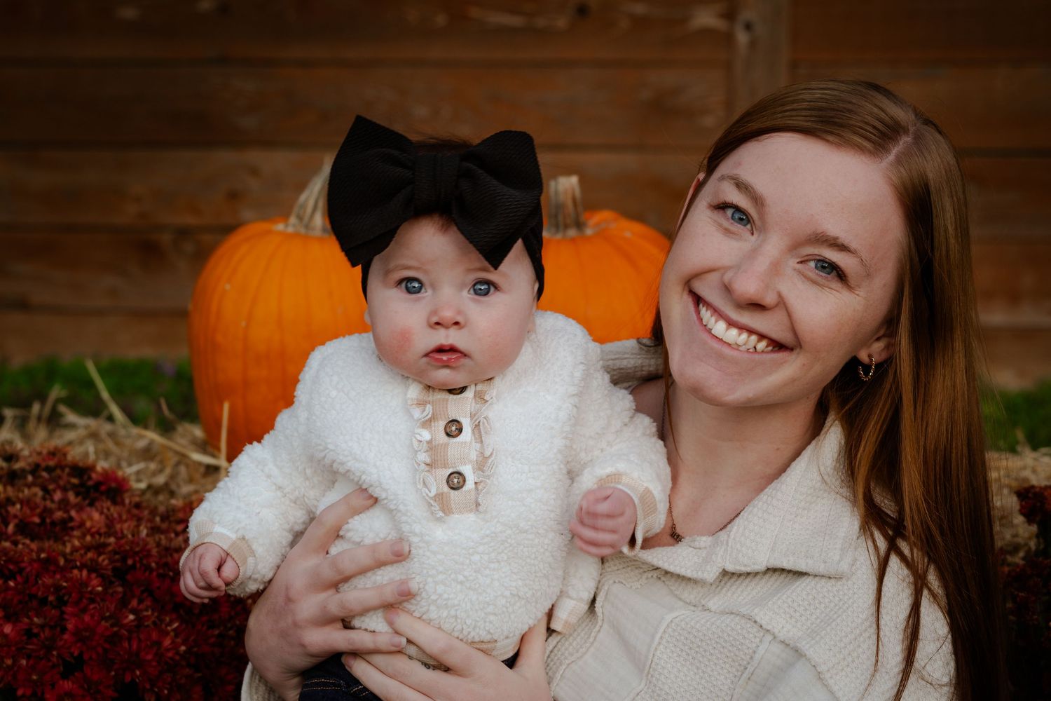 Fall family photo session outdoors with pumpkins and autumn foliage in warm brown tones.