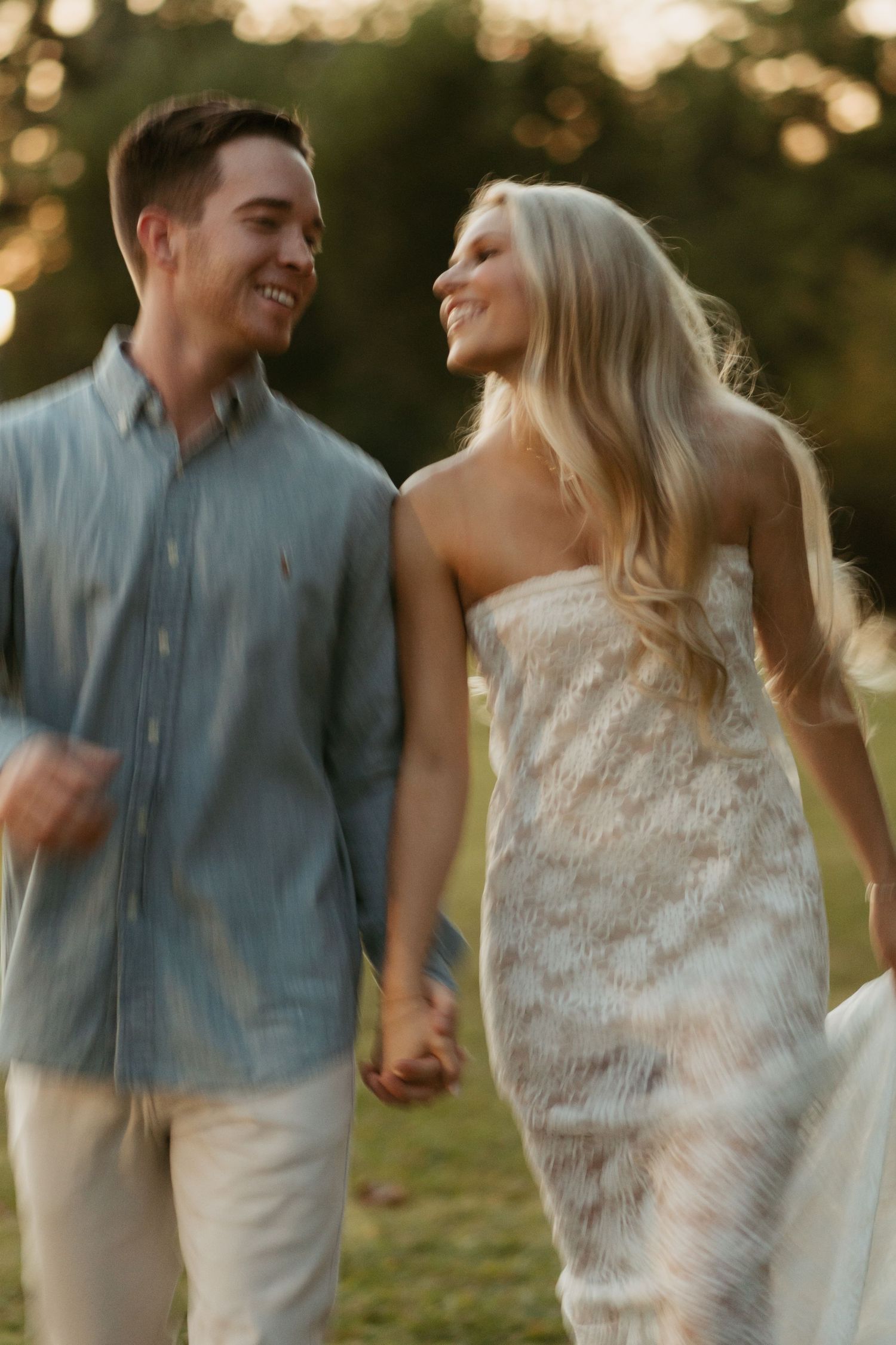 A couple laughs together during a romantic sunset photoshoot in a park while wearing coordinated blue and white outfits.
