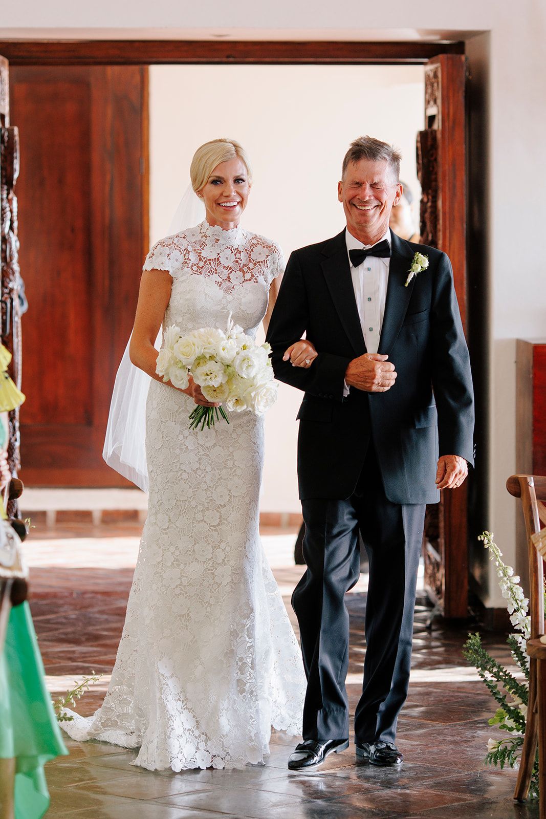 Bride in lace gown walks arm in arm with her father during a timeless ceremony in Puerto Vallarta, by José Carrillo Photography.