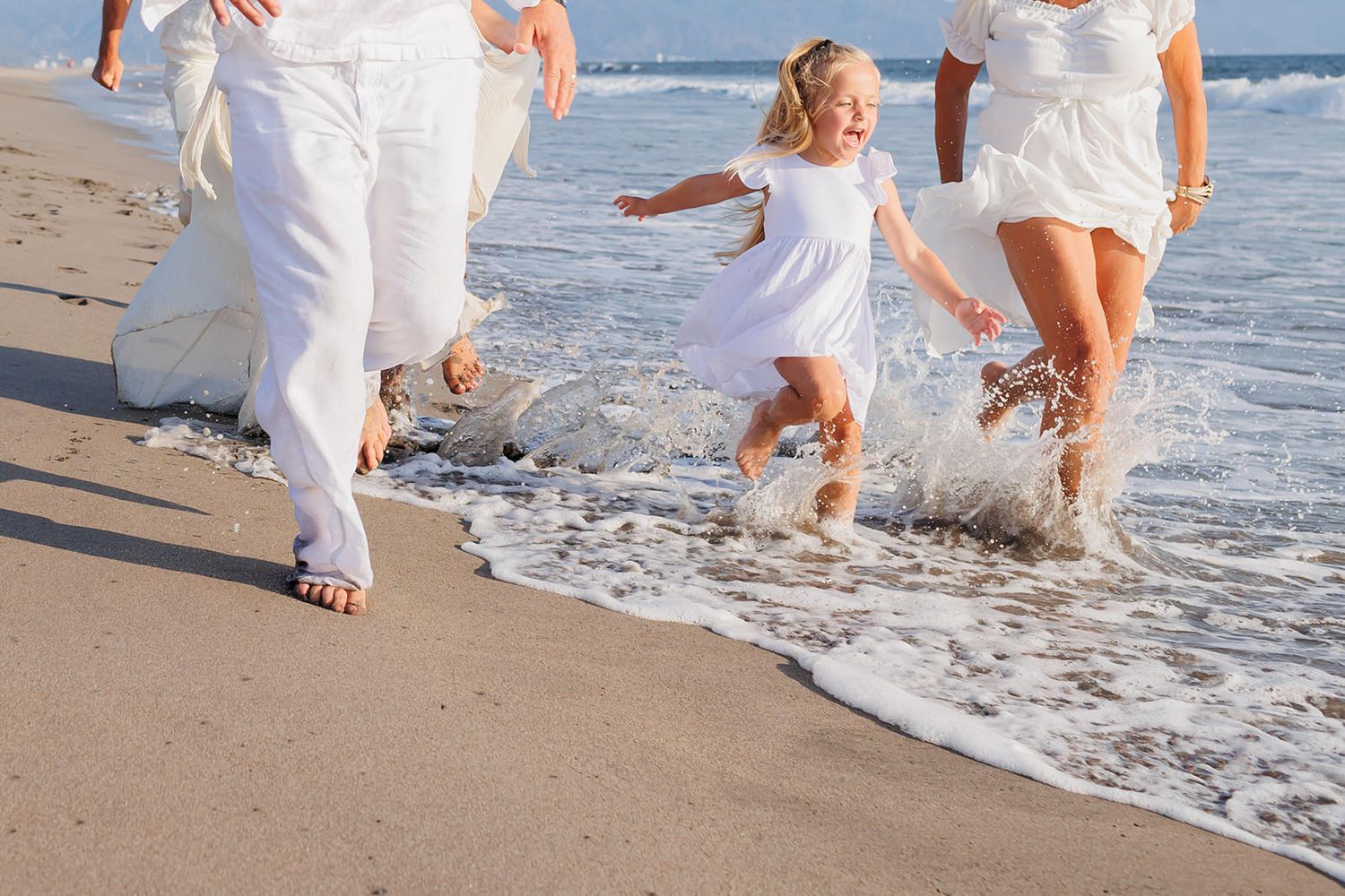 Young girl running through the ocean with her family during a beach photo session at Vidanta Nuevo Vallarta